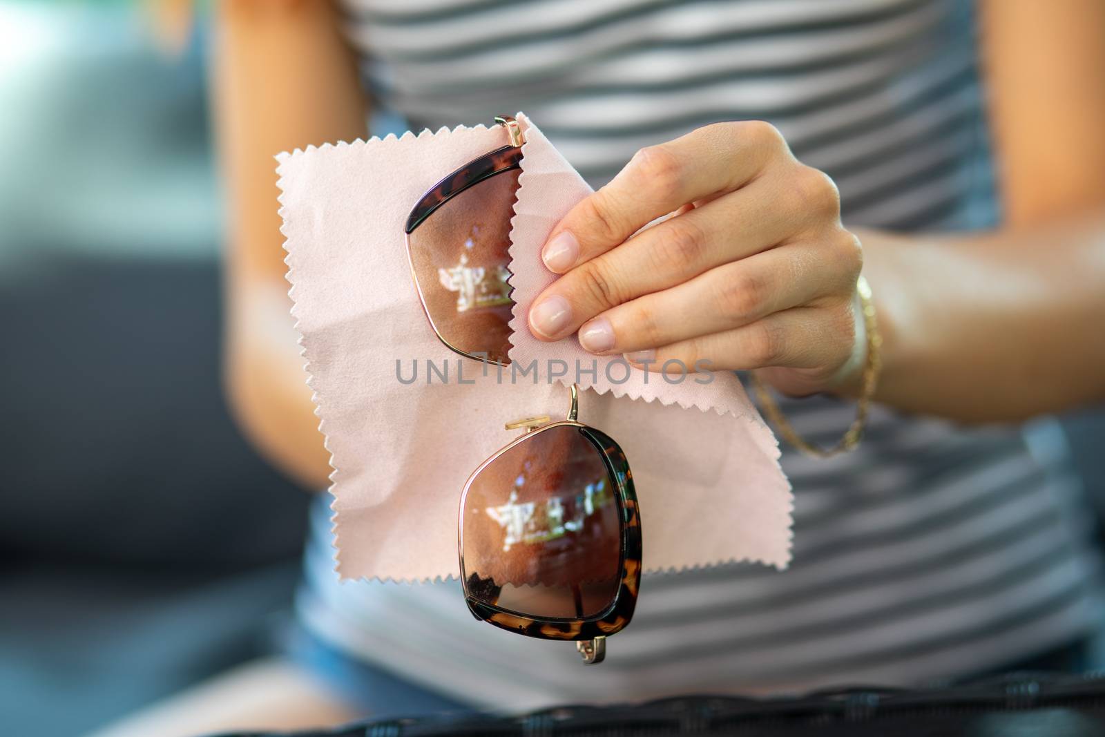 Woman hands cleaning her sun glasses with micro fiber cloth wipe, wipping sunglasses