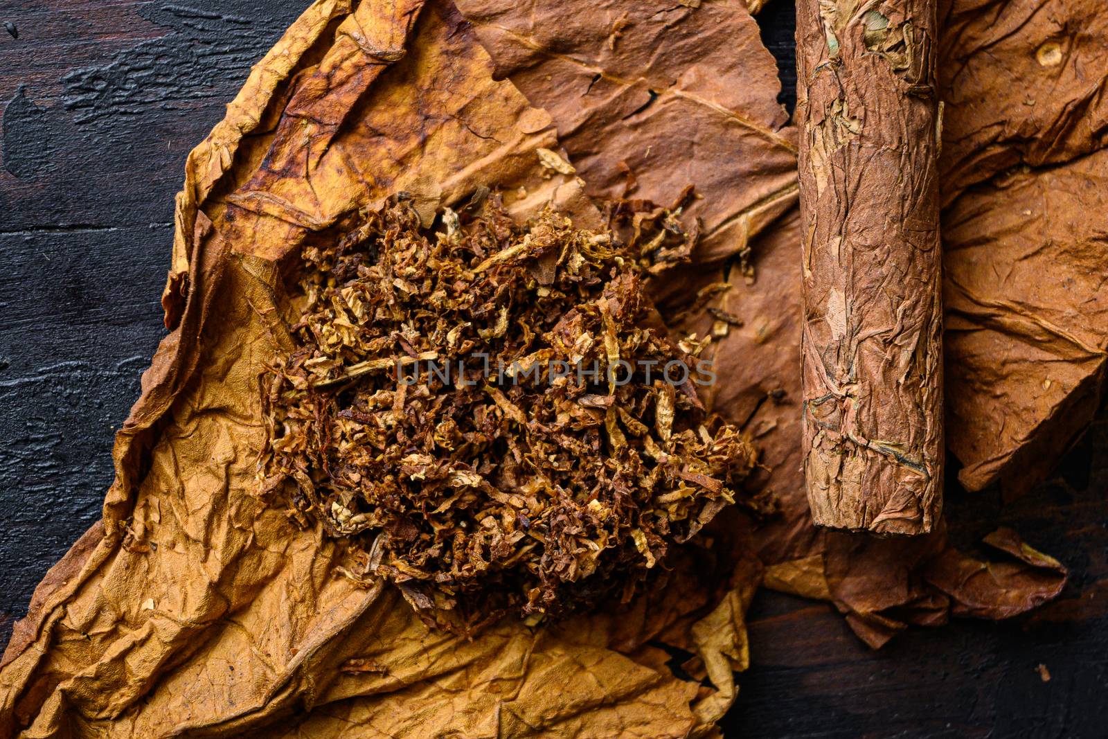 Close-up of cigar and pile of tobacco and dried tobacco leaf on wood background dark top view.