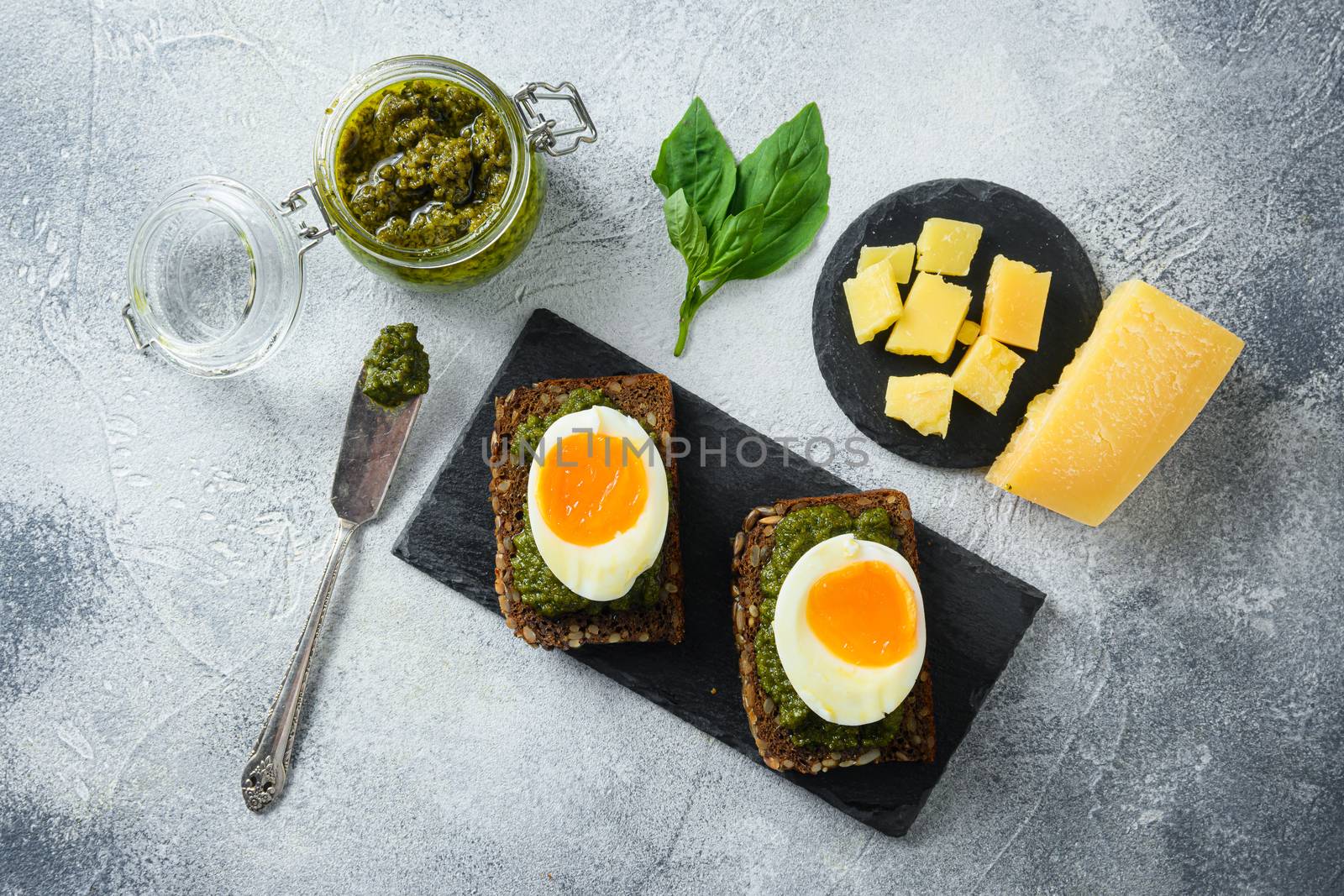 homemade eggs panini bread with Green basil pesto silver spoon on italian breakfast with ingredients green pesto on grey and white concrete table surface top view .