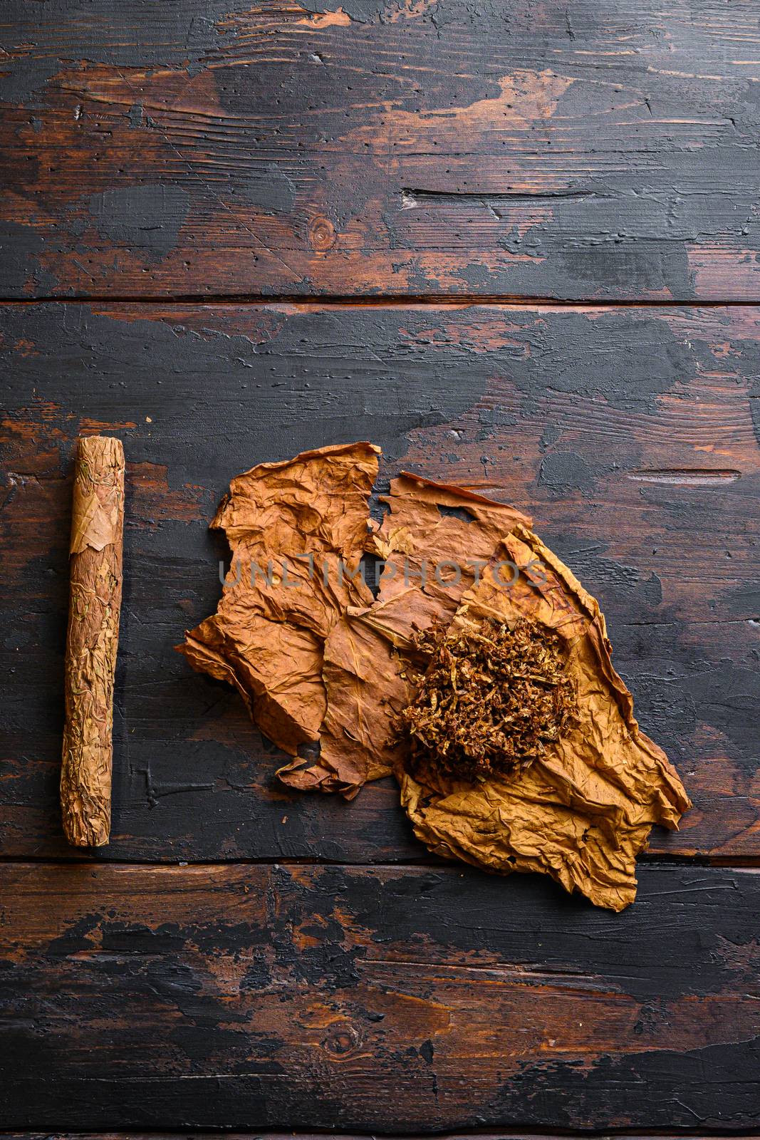 Cut tobacco and tobacco leaves with cigar on background on vintage dark table. overhead shot top view space for text.