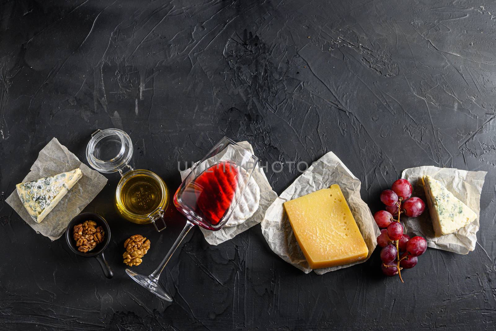 Assortment of cheeses, Camembert antipasto a glass of red wine, honey, nuts and spices, on a black backdrop stone slate Top view. Free space for text top view by Ilianesolenyi
