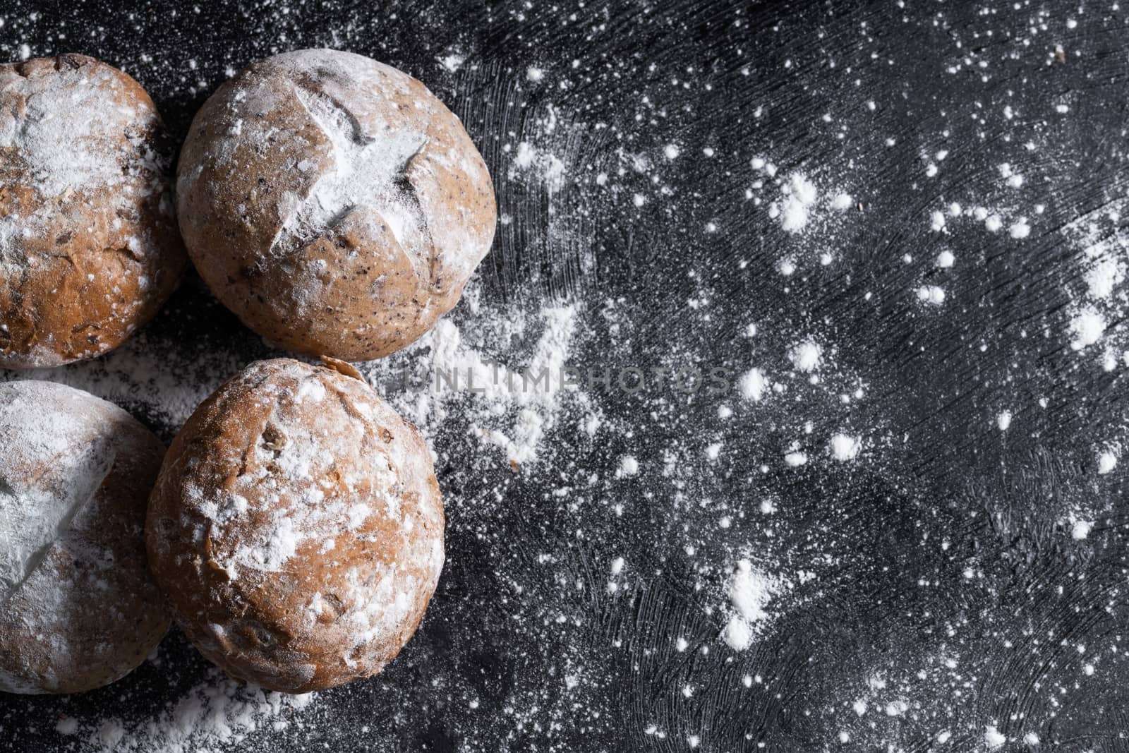 Close-up a rustic loaves of bread and filled with flour sprinkled on a black wooden table.