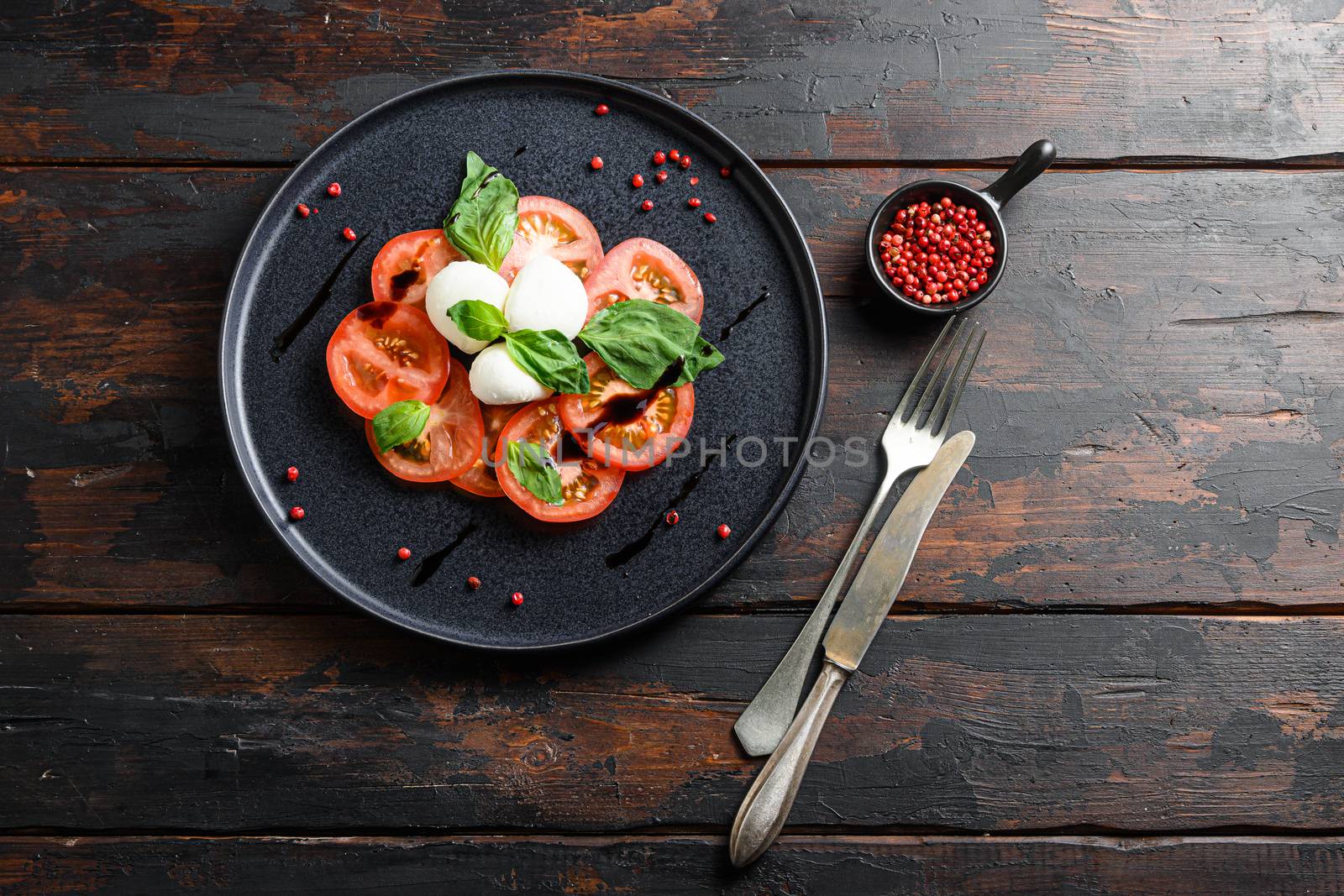 caprese salad with sliced tomatoes, mozzarella cheese, basil, olive oil. Served on black plate wood kitchen old rustic table top view flatlay space for text by Ilianesolenyi