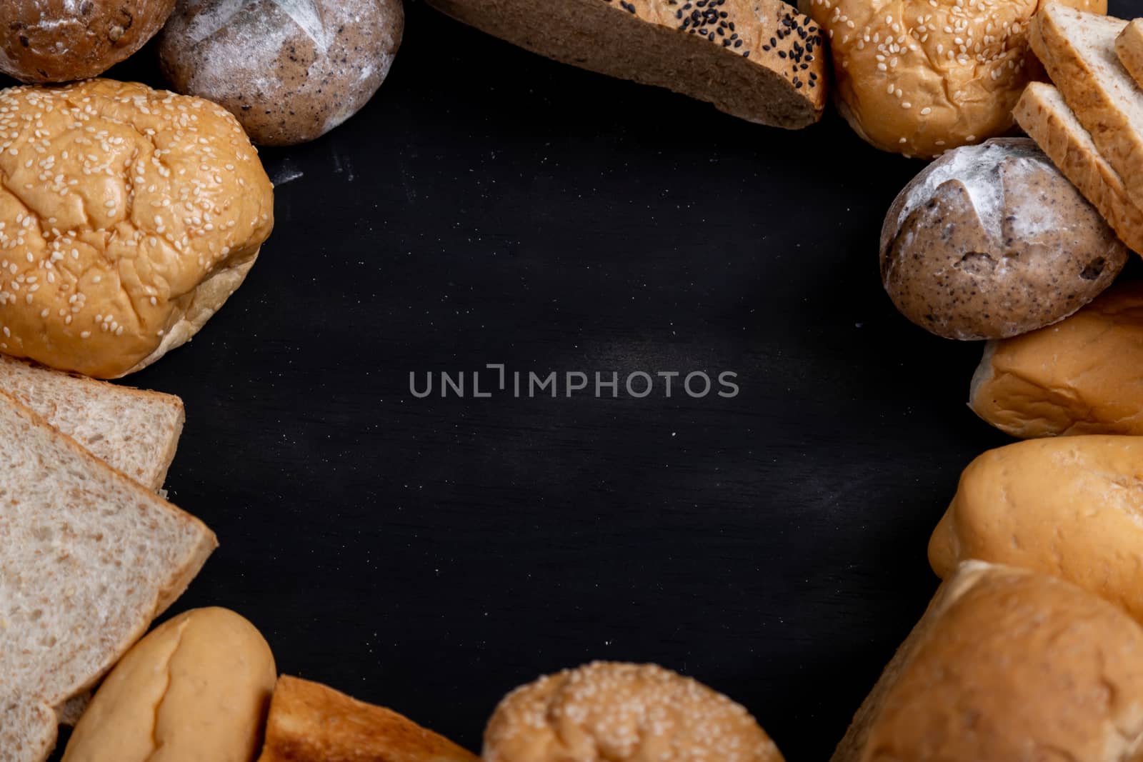 Various kinds of bread placed on the black wooden background in a circle and leave a space in the center for the text.