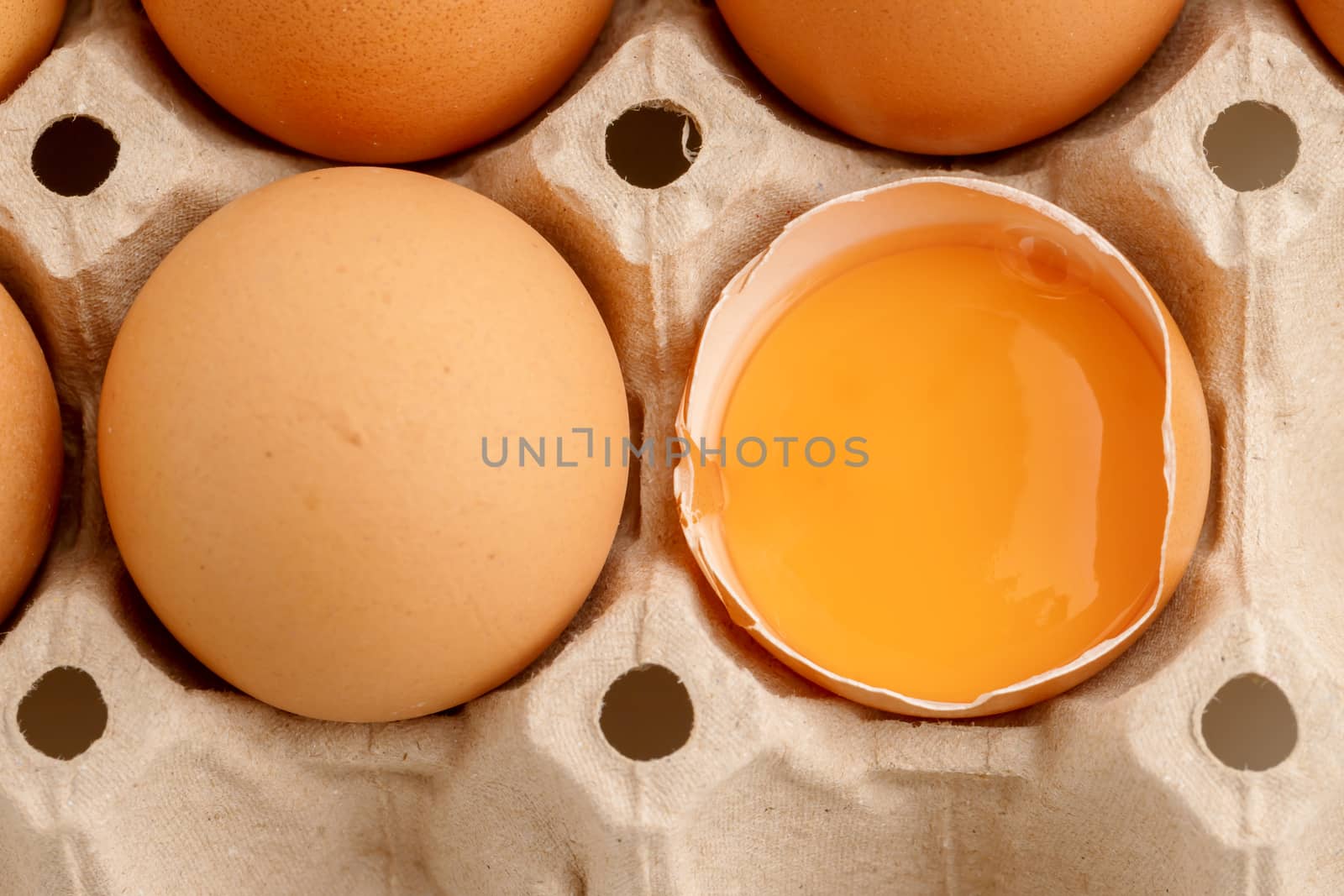 Top view has broken egg with the yolk in the paper carton.