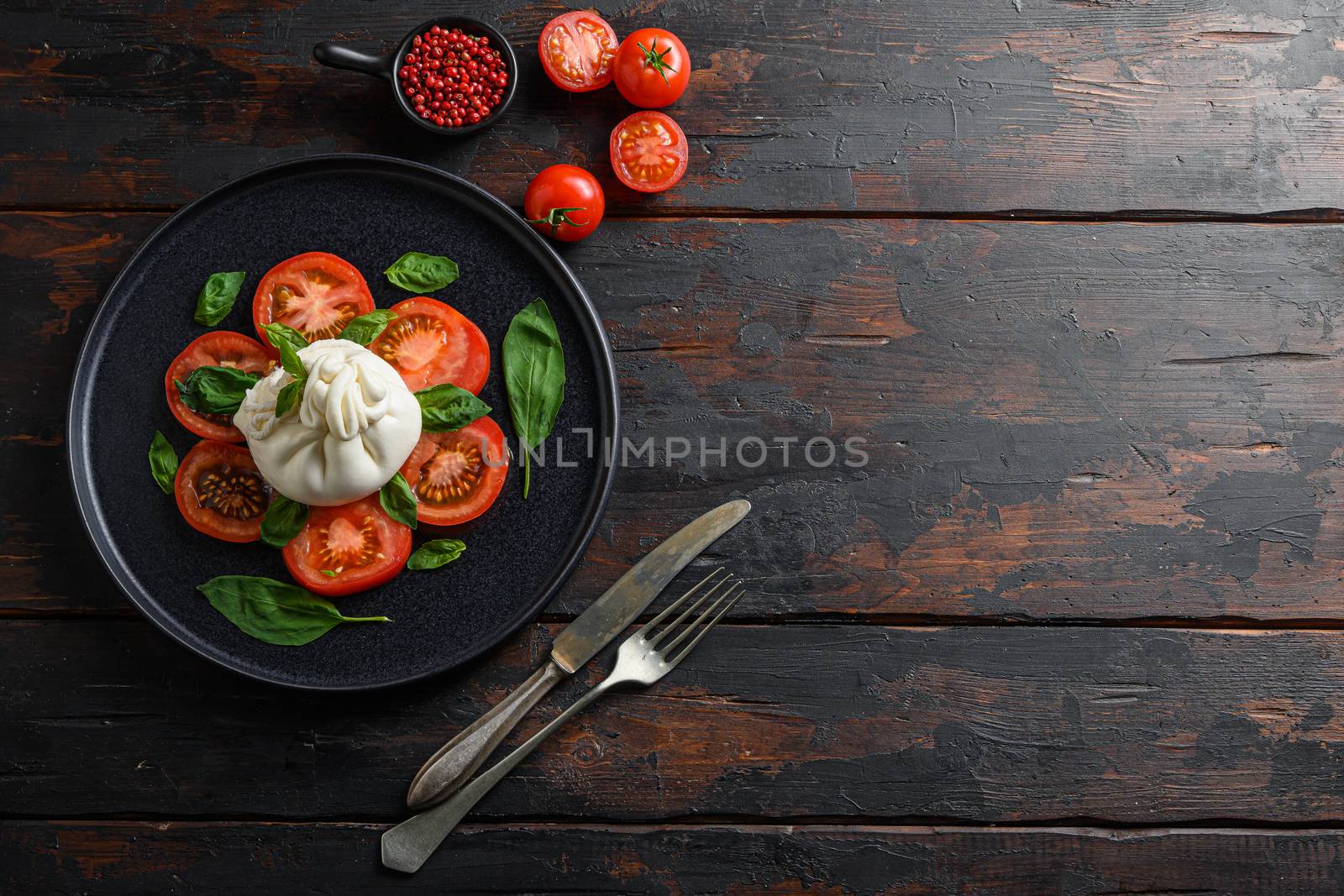 Burrata, Italian fresh cheese made from cream and milk of buffalo or cow. on black plate old wood table planks top view space for text old knife and fork.