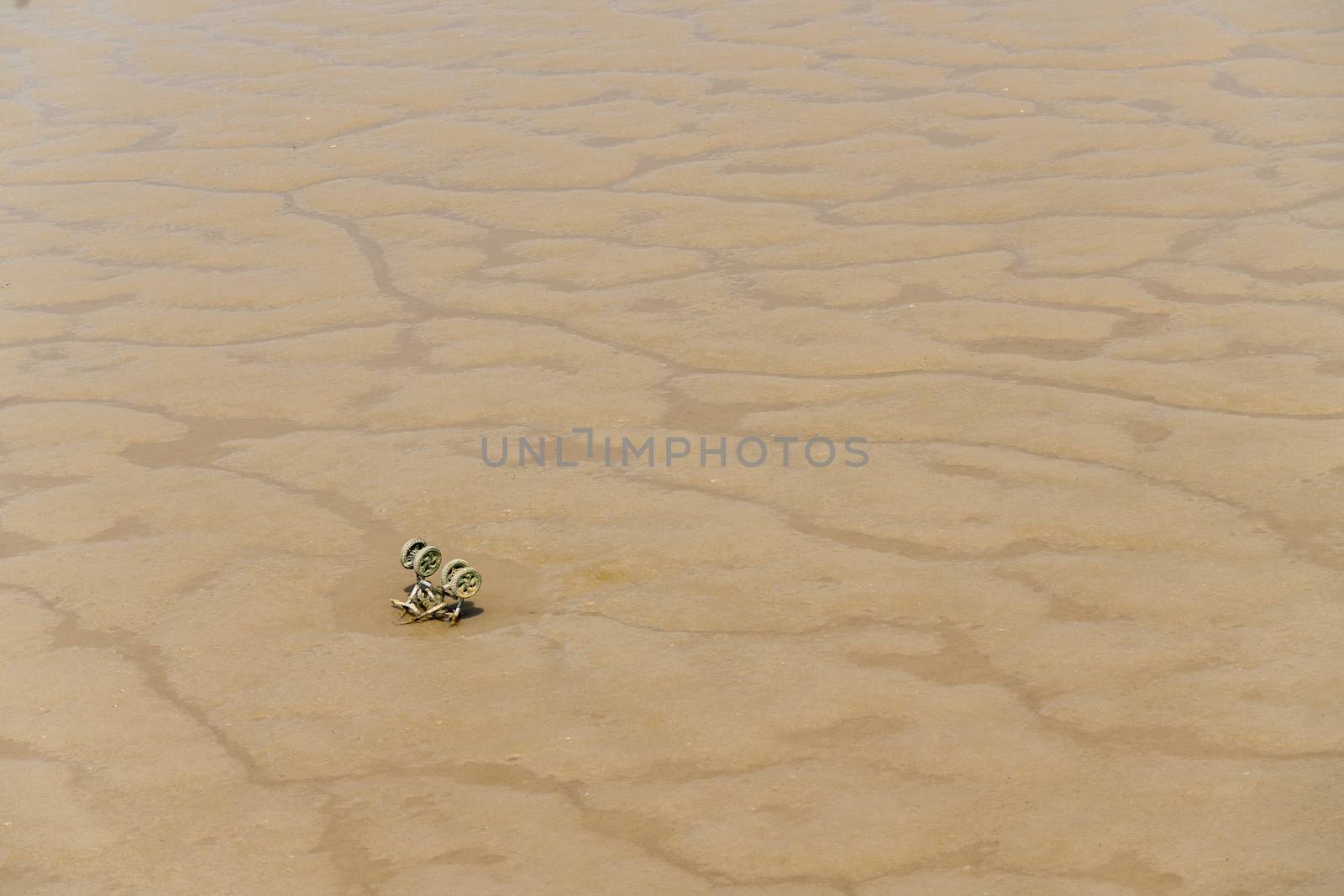 Abandoned and sinking childs stroller or pushchair in sandy mud of riverbank
