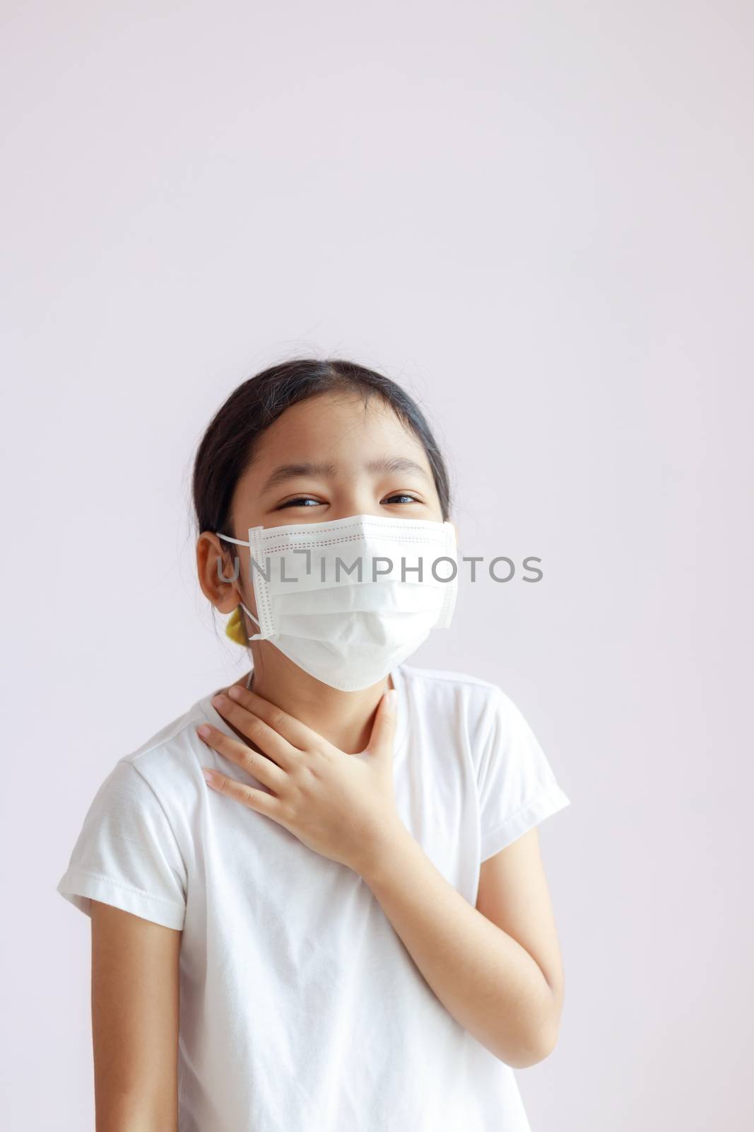 Portrait of little Asian girl touching her neck with a sore throat. The child wears a sanitary mask. The epidemic of the flu, Coronavirus or COVID-19 and illness.
