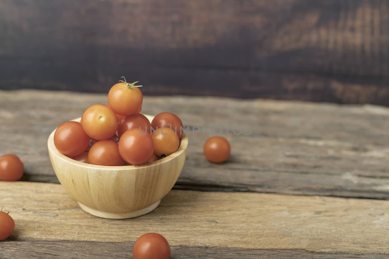 Cherry tomatoes in a wood bowl place on the wooden table by Nikkikii