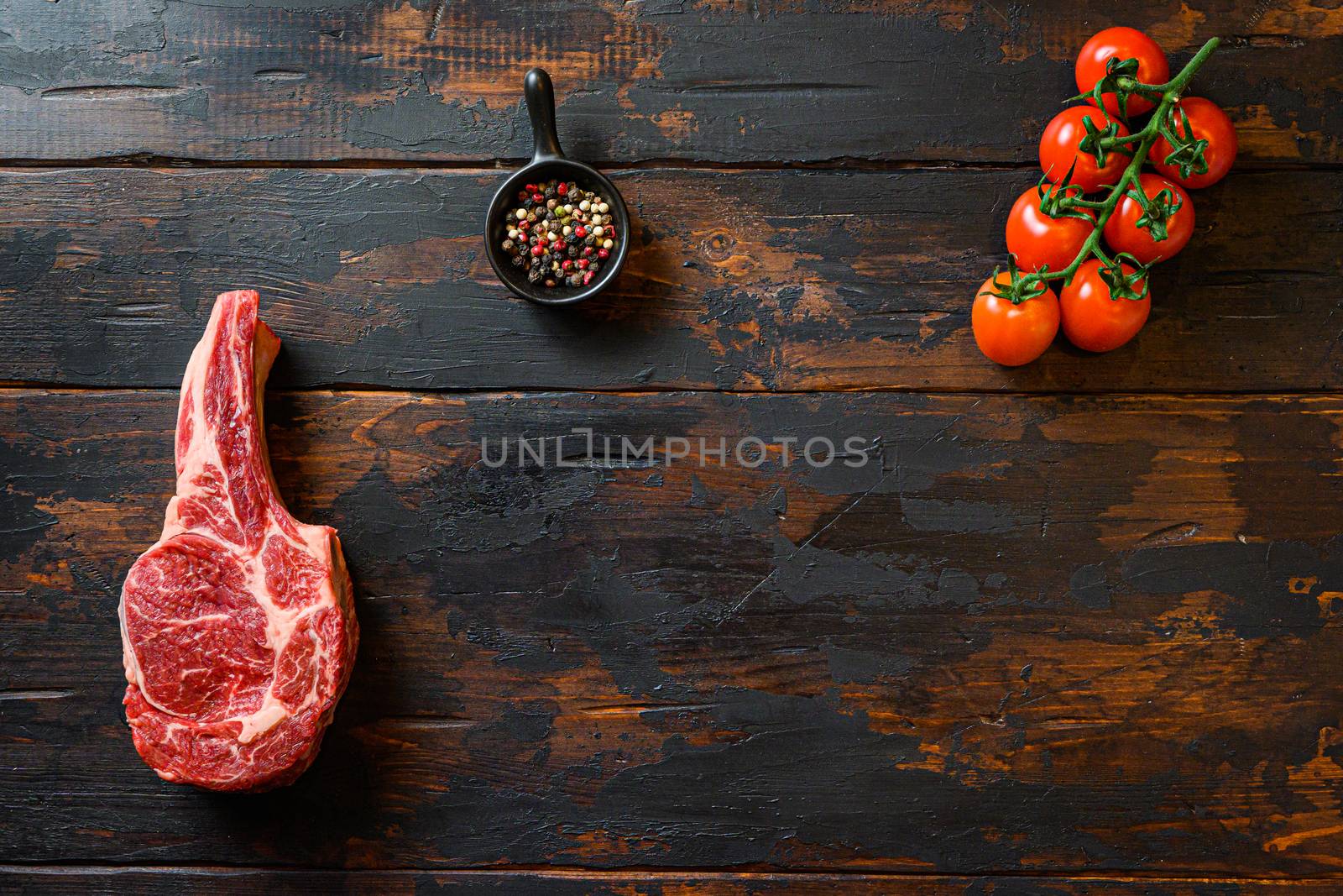 Cowboy beef steak, and spices with tomatoes on a rustic wooden table dark background. Top view with copy space for your text