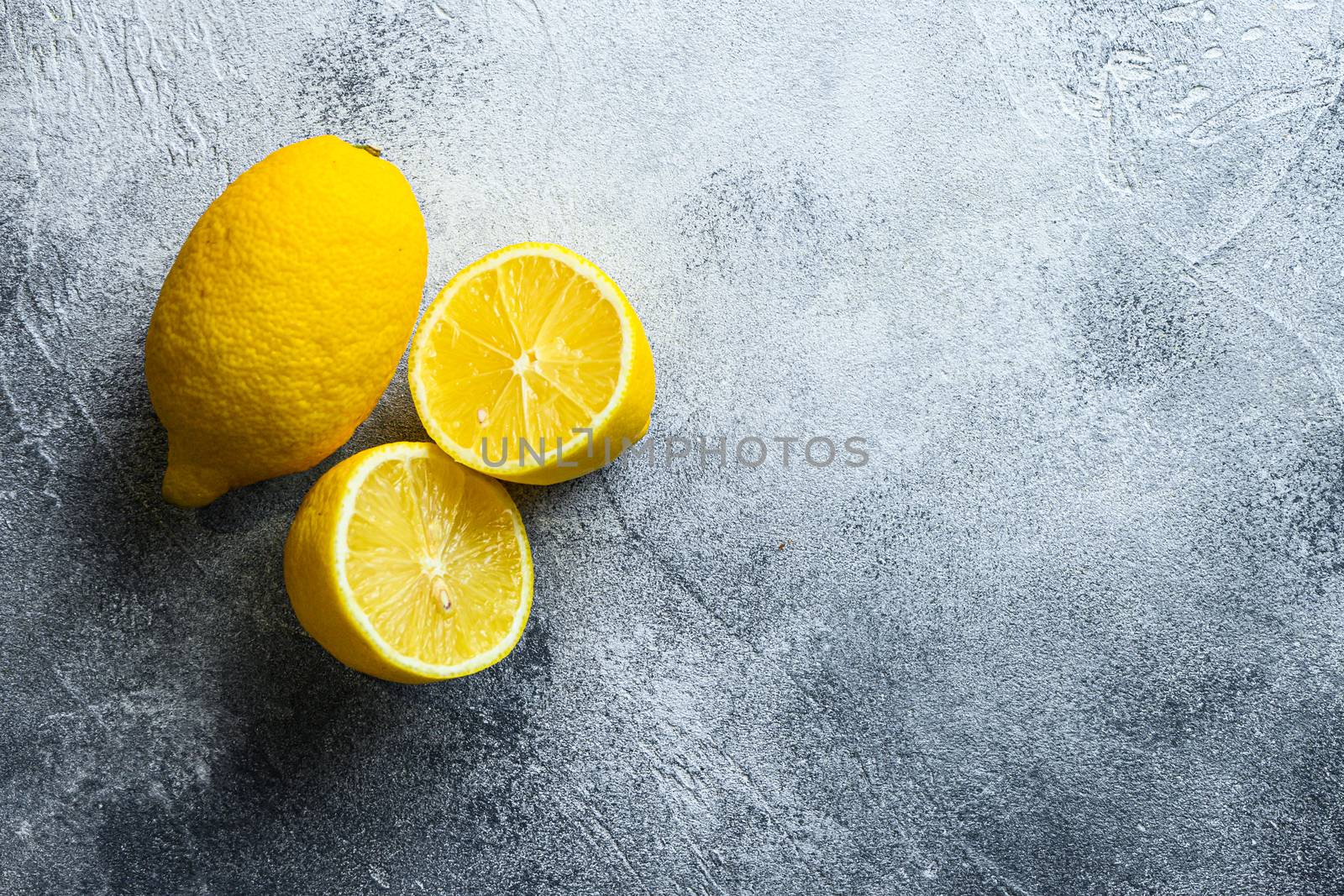 Whole and liced half fruit lemon and on grey background with space for text.