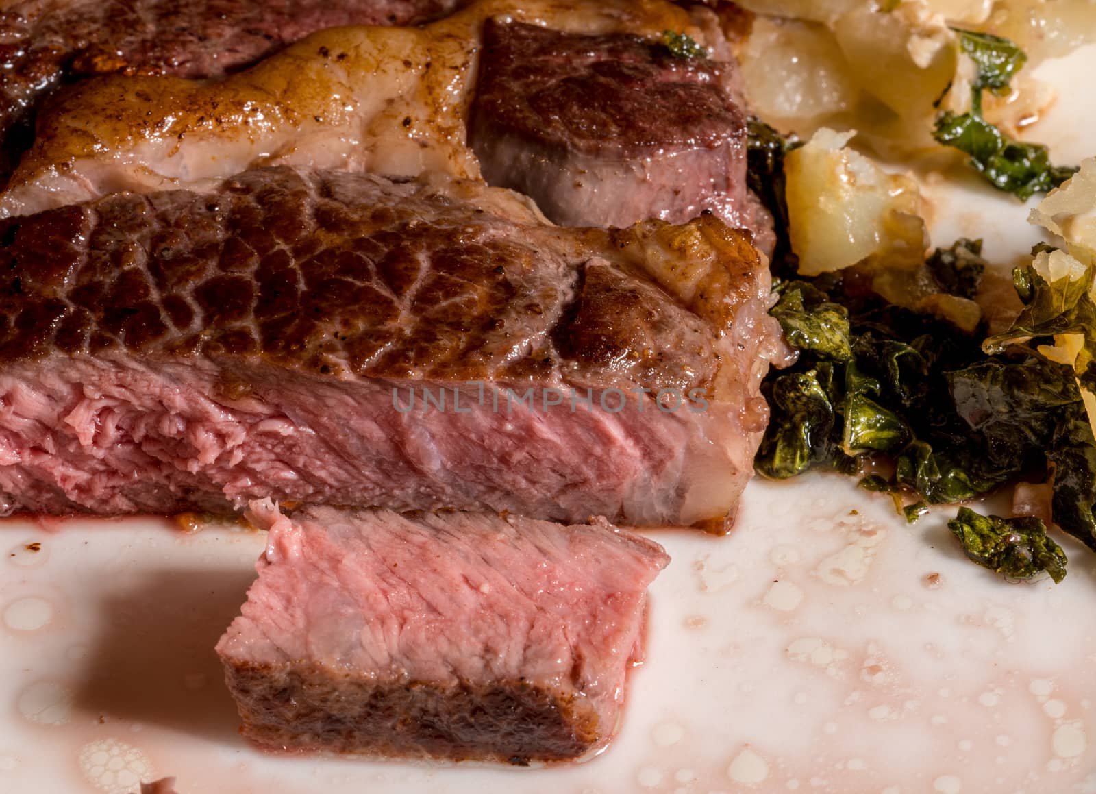 Large grilled ribeye steak with slice on white plate with roasted kale and sliced potatoes