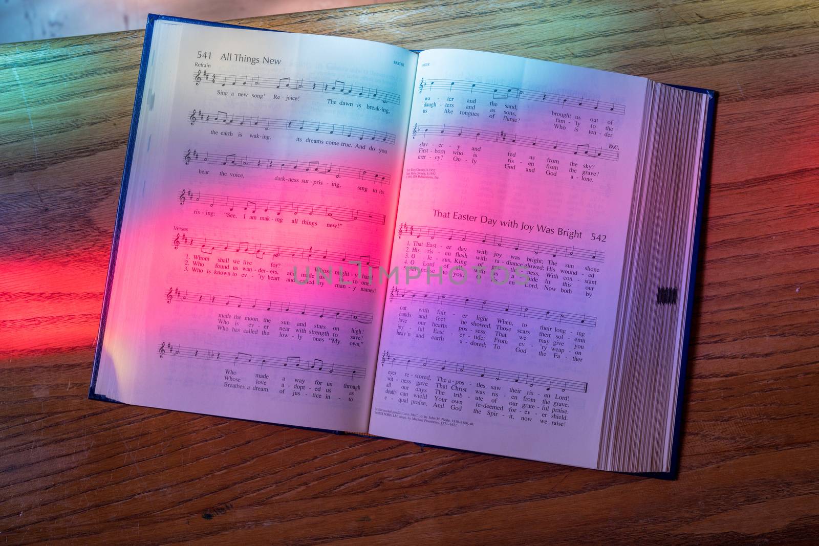 Colored light from stained glass window in methodist church falls across open hymnal for Easter hymn