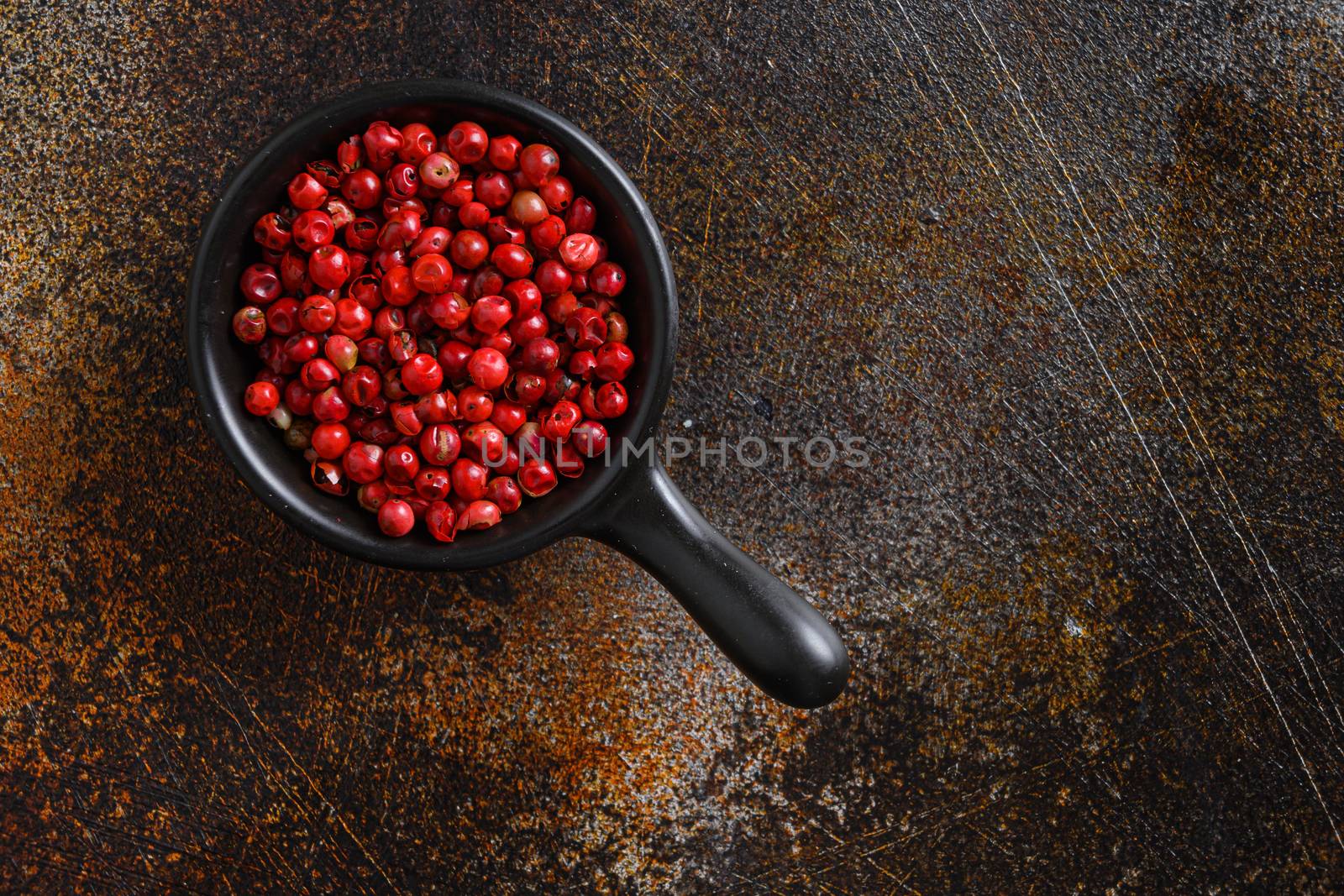 Close-up image of pepper rose, pink peppercorns on black wood background, view above space for text on side.