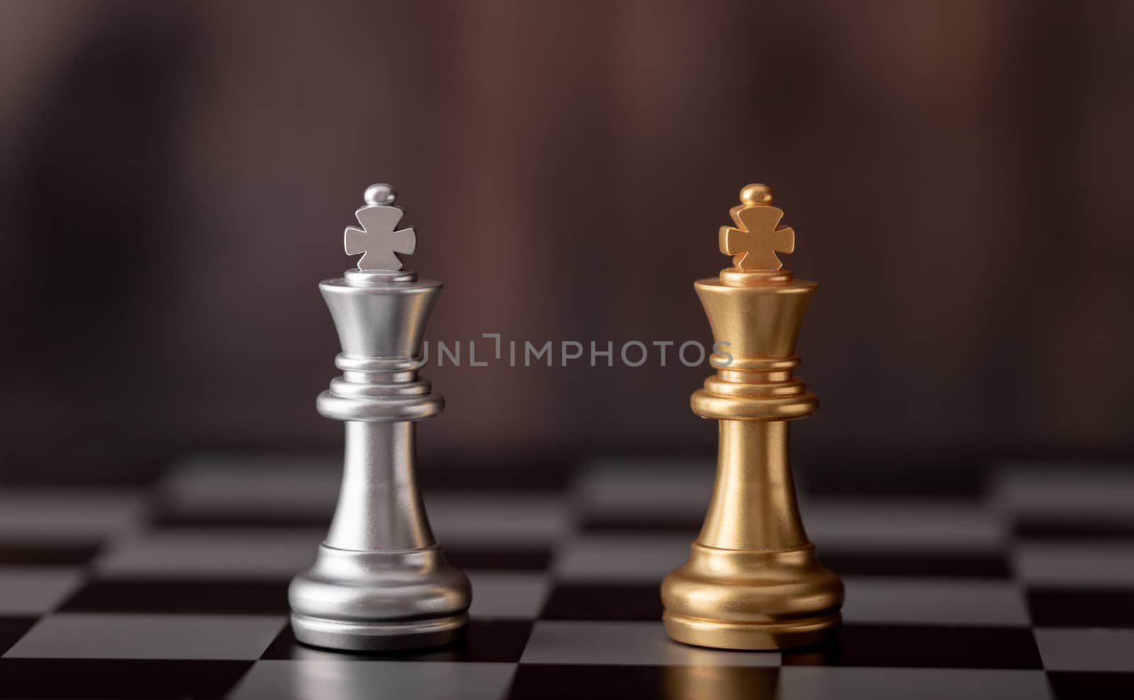 gold and silver king standing on chess board with wooden background