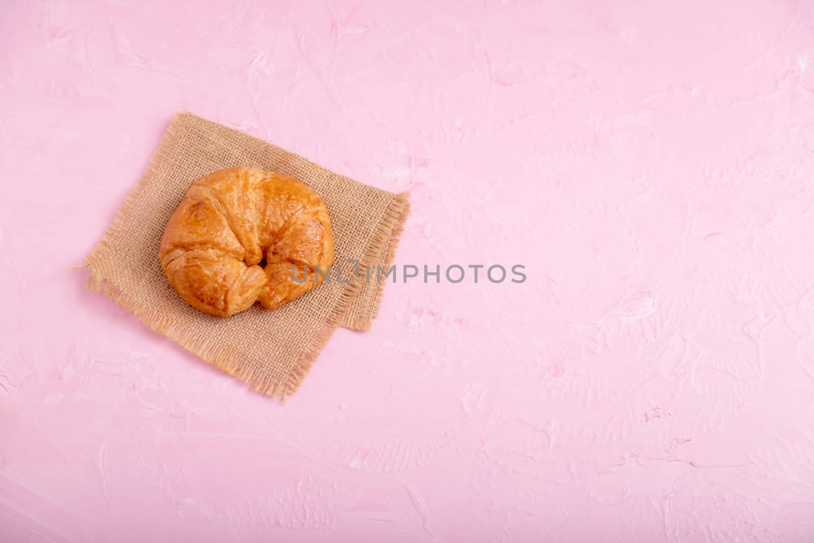 Top view croissant on the brown sack. Bread on the pink background and texture.