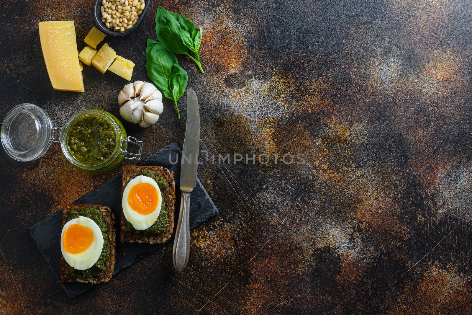 homemade eggs panini bread with Green basil pesto in glass jar silver spoon on italian breakfast with ingredients green pesto on gmetal surface table top view space for text.