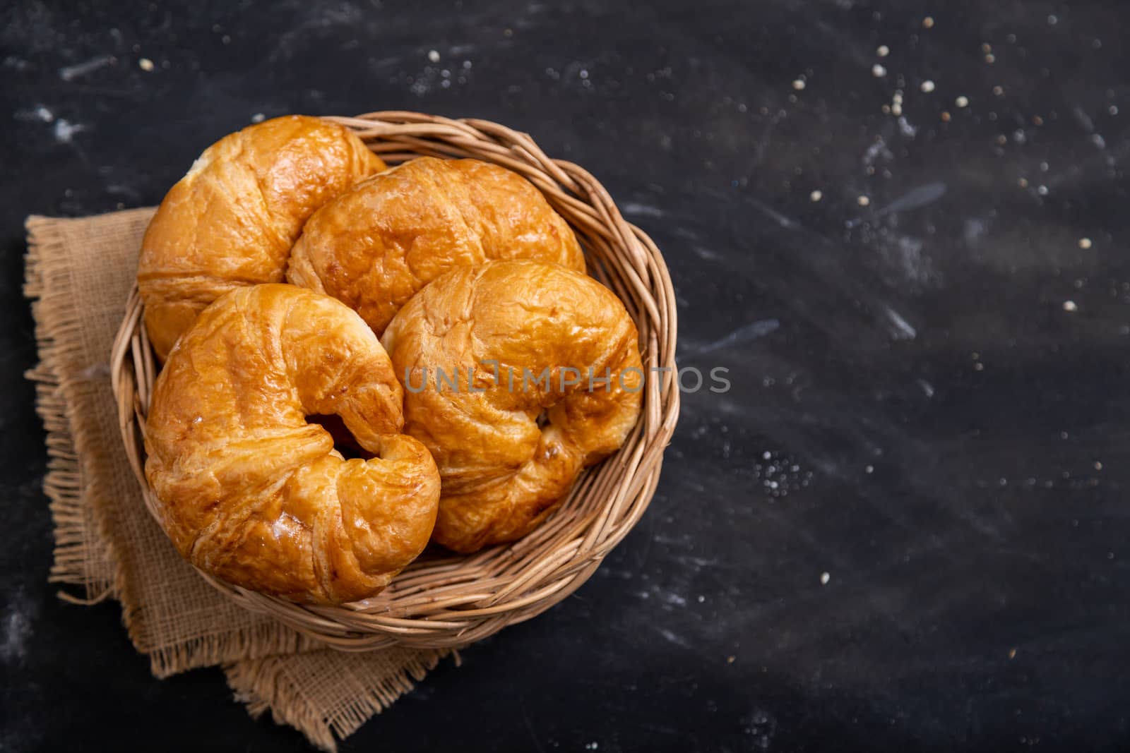 Top view Croissant in a wicker basket placed on a black floor by Nikkikii