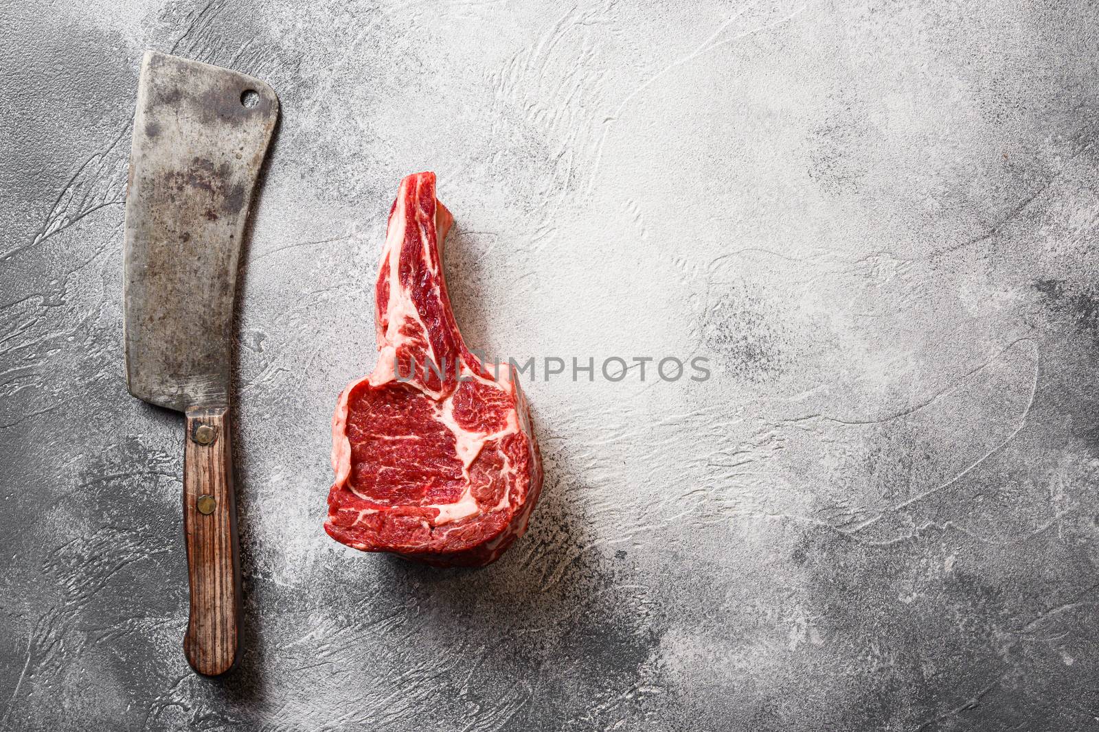 Raw black angus Cowboy steak or Dallas steak cut with the meat american cleaver knife over grey stone table slate cutting top view. Space for text.