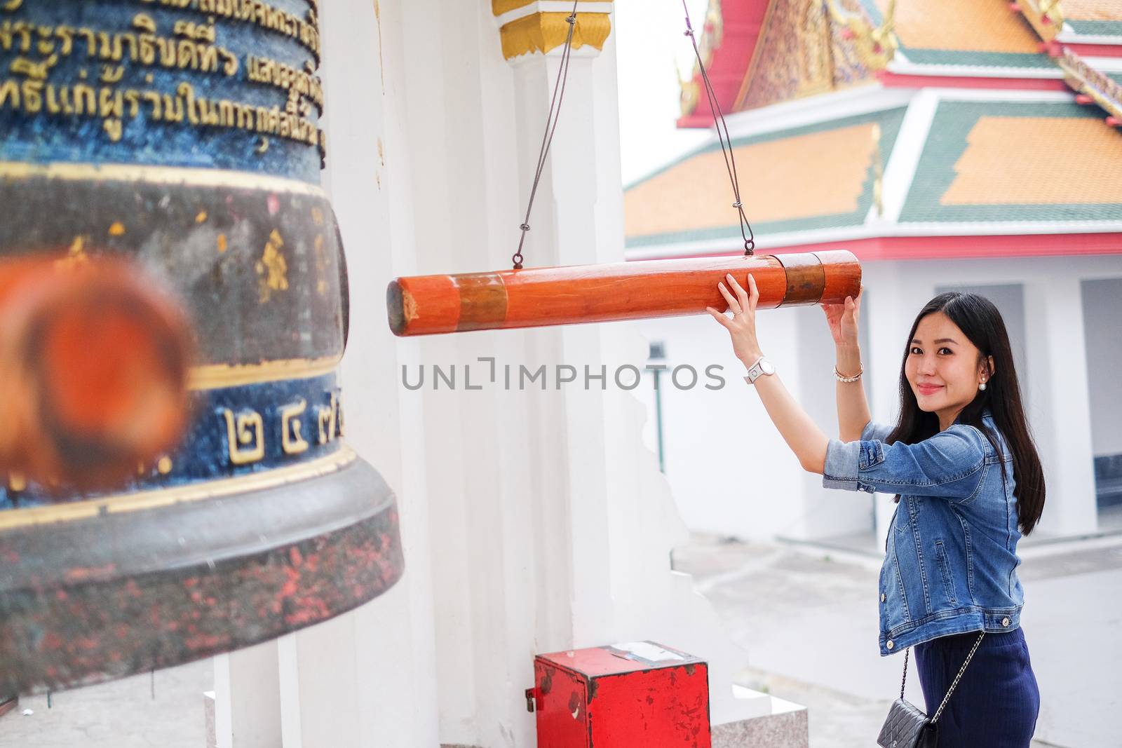 Woman ringing a bell in a Buddhist temple in Thailand by Surasak