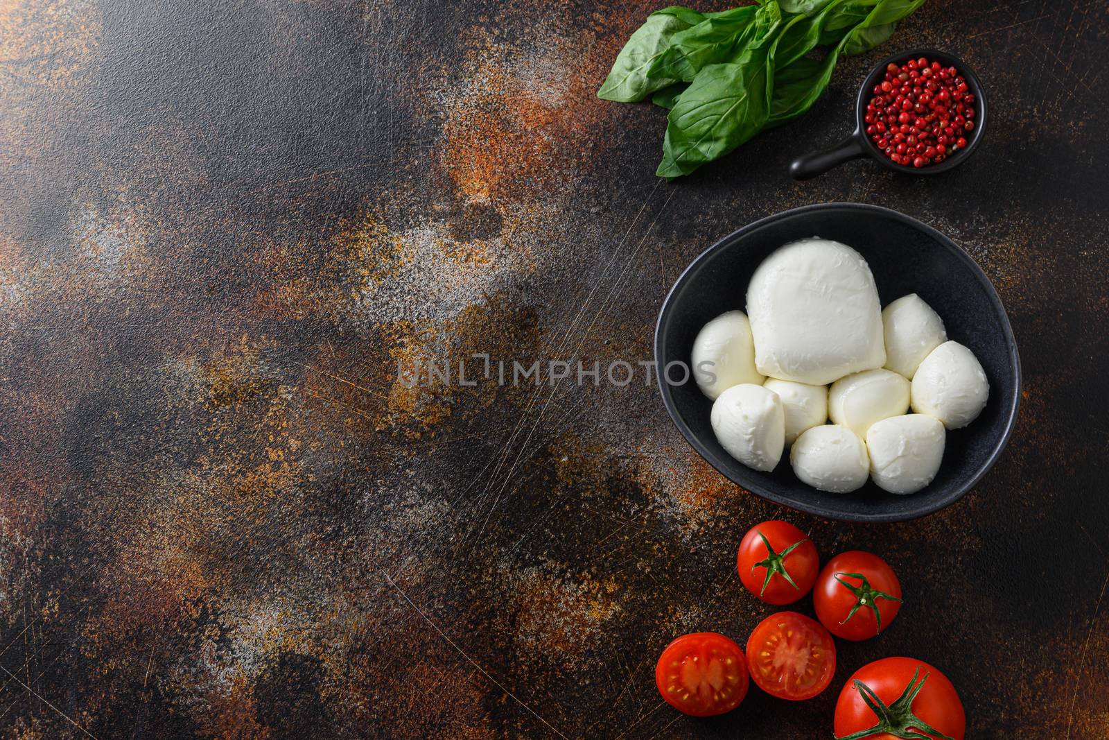 Fresh cherry tomatoes, basil leaves, mozzarella cheese and olive oil on old rustic metal background. Caprese salad ingredients. Selective focus. top view space for text by Ilianesolenyi