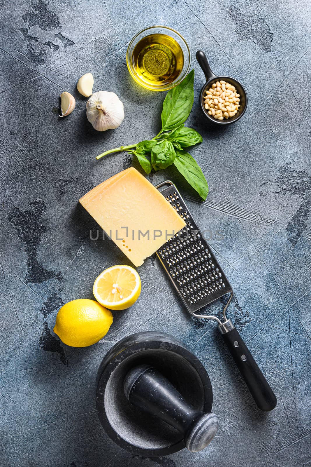 Pesto genovese sauce Ingredients italian recipe Fresh basil, tomatoes mortar lemon olive oil parmesan pine nuts on the stone table on gray concrete background Top view by Ilianesolenyi