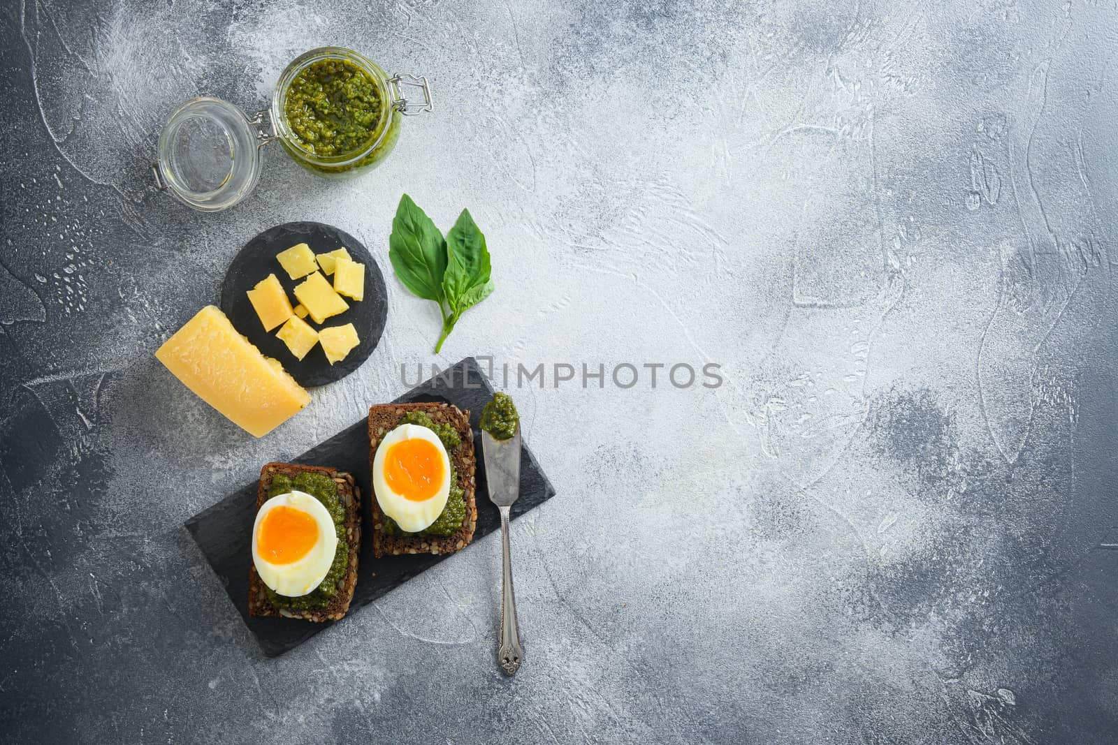 homemade eggs panini bread with Green basil pesto silver spoon on italian breakfast with ingredients green pesto on grey and white concrete table surface overhead top view space for text lay flat by Ilianesolenyi