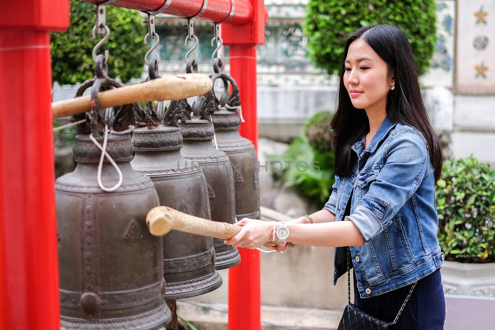 Woman ringing a bell in a Buddhist temple in Thailand by Surasak