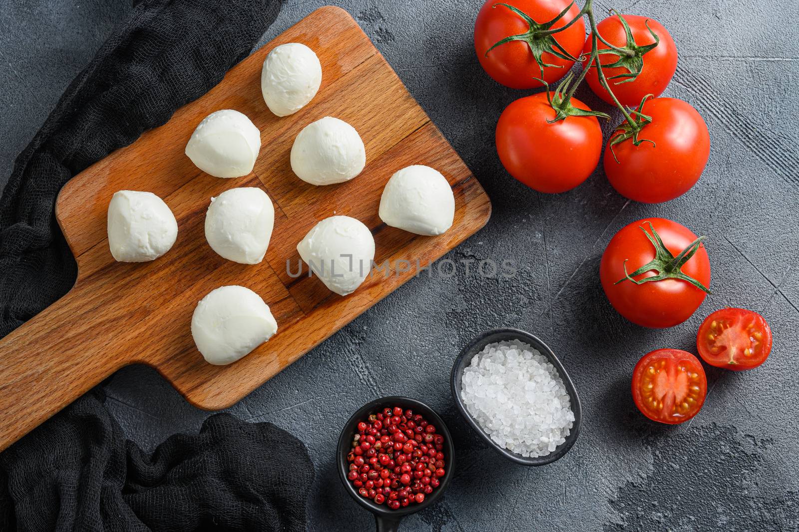 Buffalo Mozzarella cheese balls with fresh basil leaves and cherry tomatoes, the ingredients of the Italian Caprese salad, on a black cloth and grey concrete background by Ilianesolenyi
