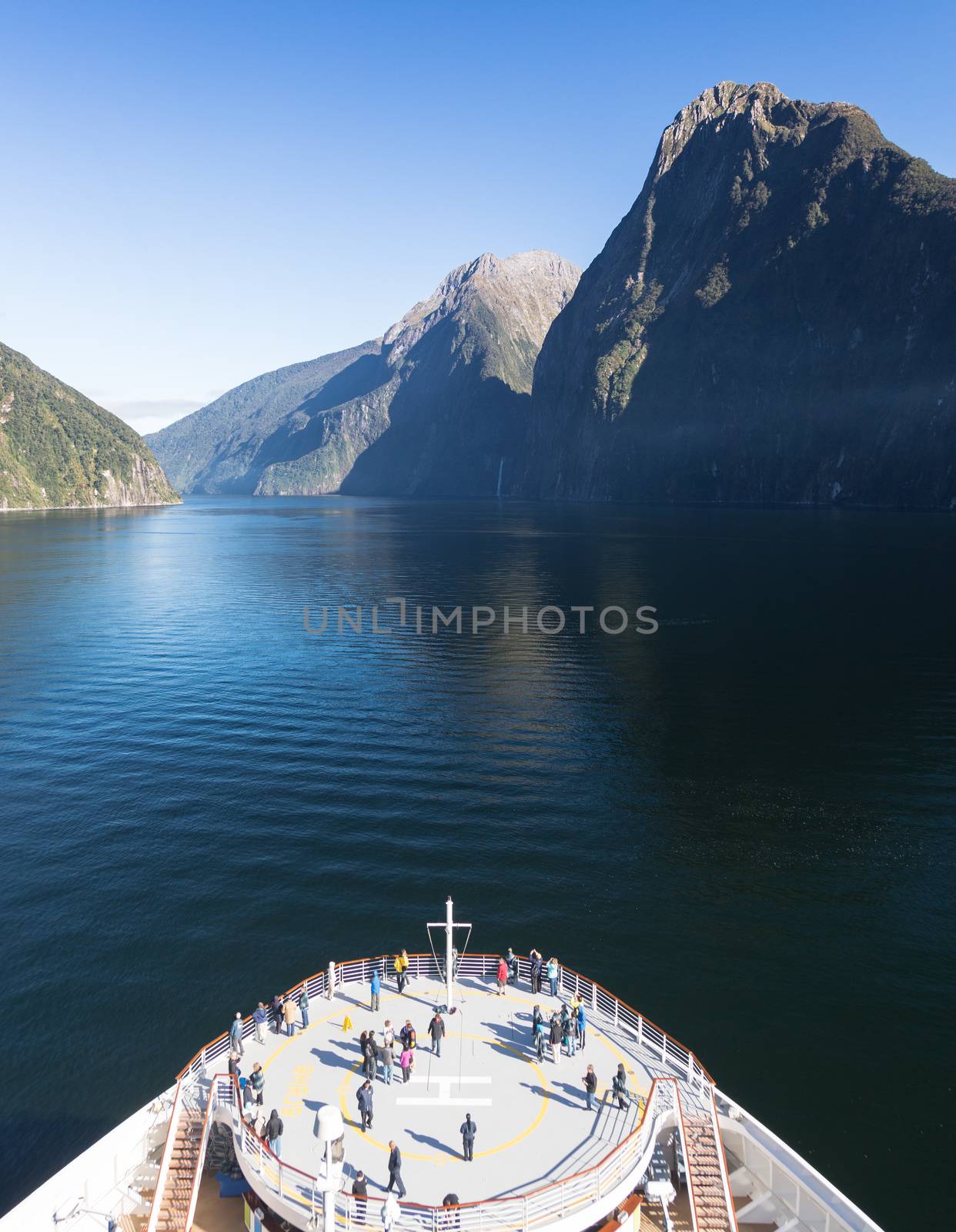 Passengers on cruise ship sailing into Milford Sound on South Island of New Zealand in early morning as the sun rises above the mountains