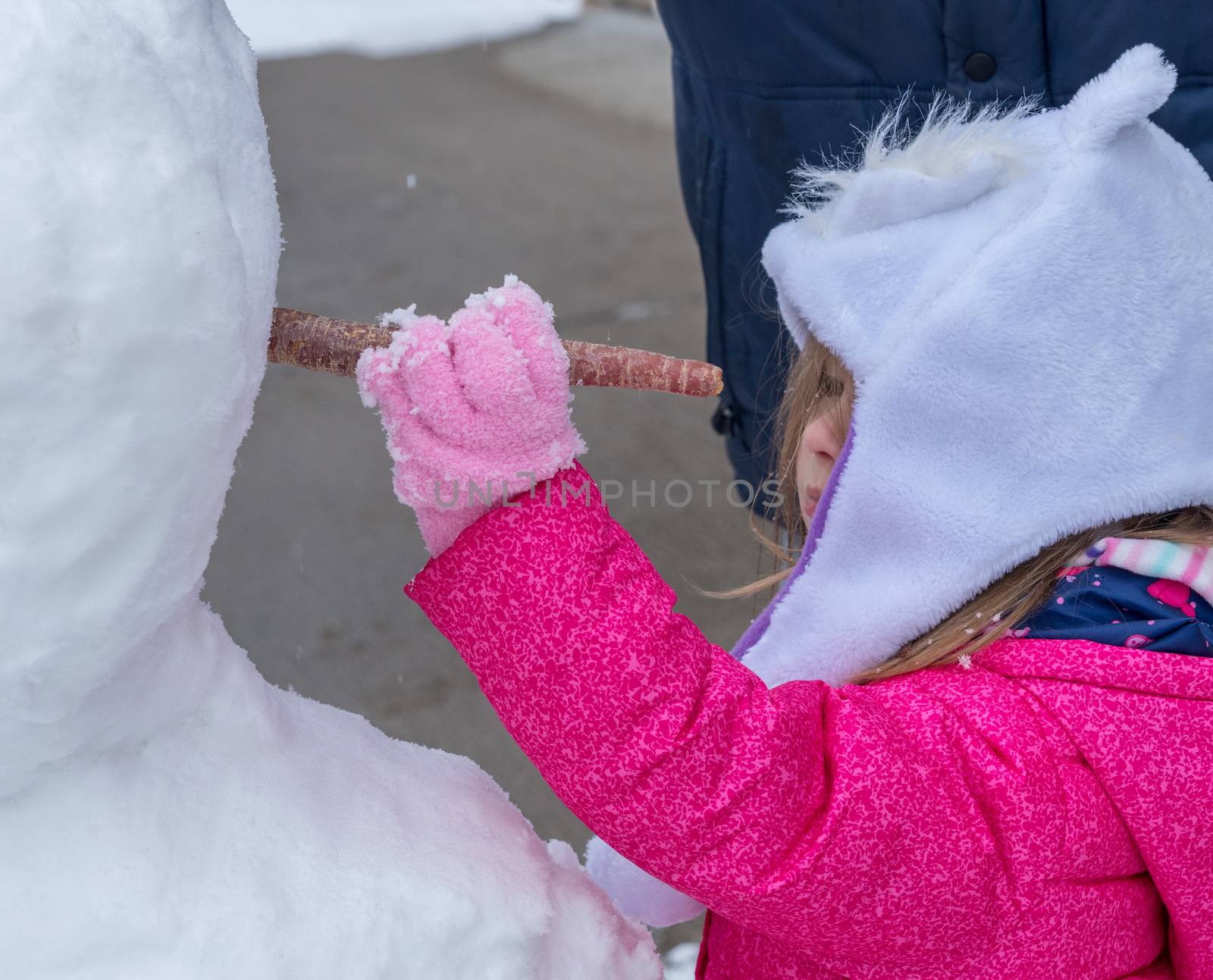 Toddler girl placing carrot into snowman face by steheap