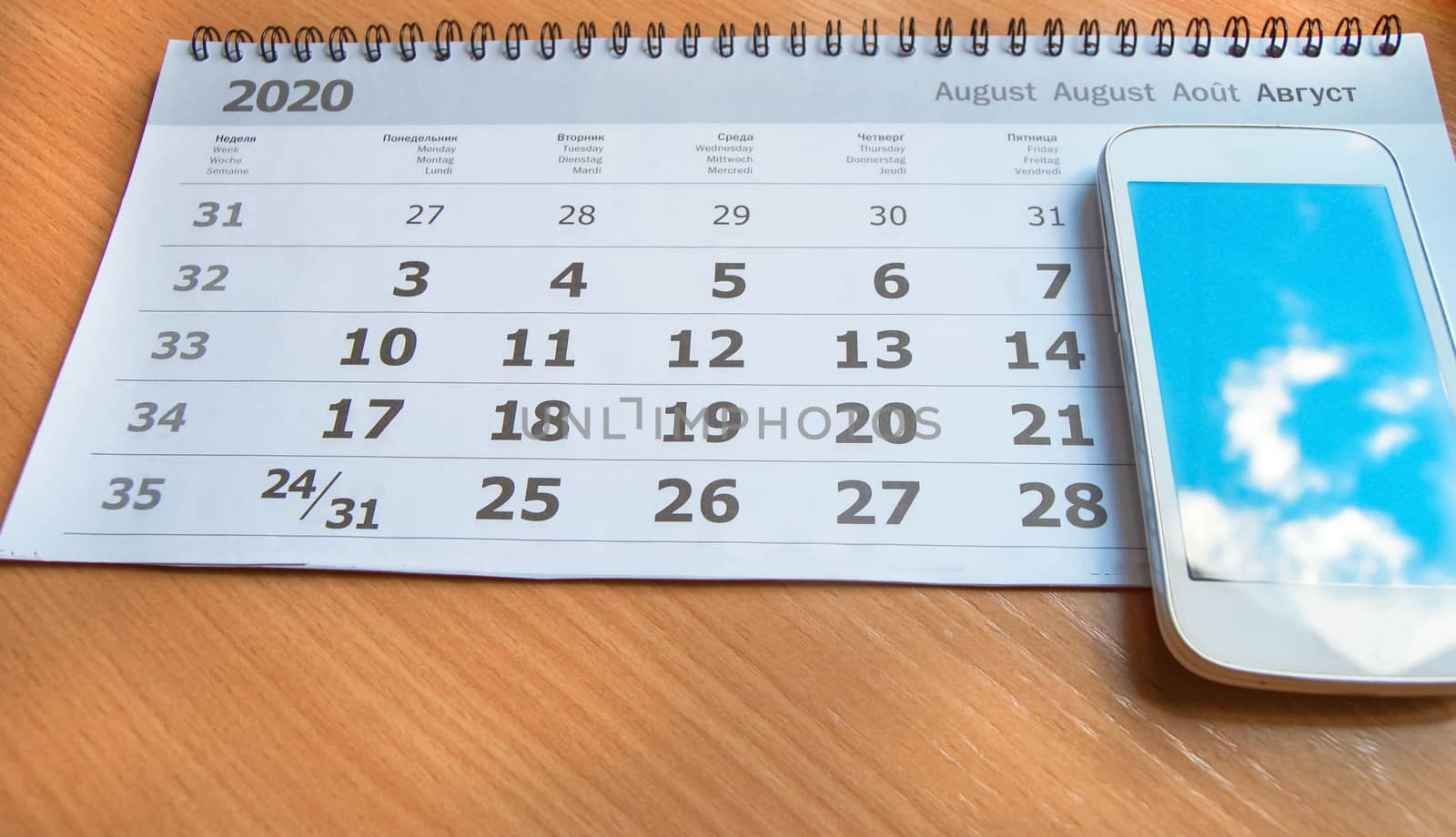 Calendar August 2020, mobile phone with reflection of clouds and blue sky on the screen, post-pandemic concept by claire_lucia