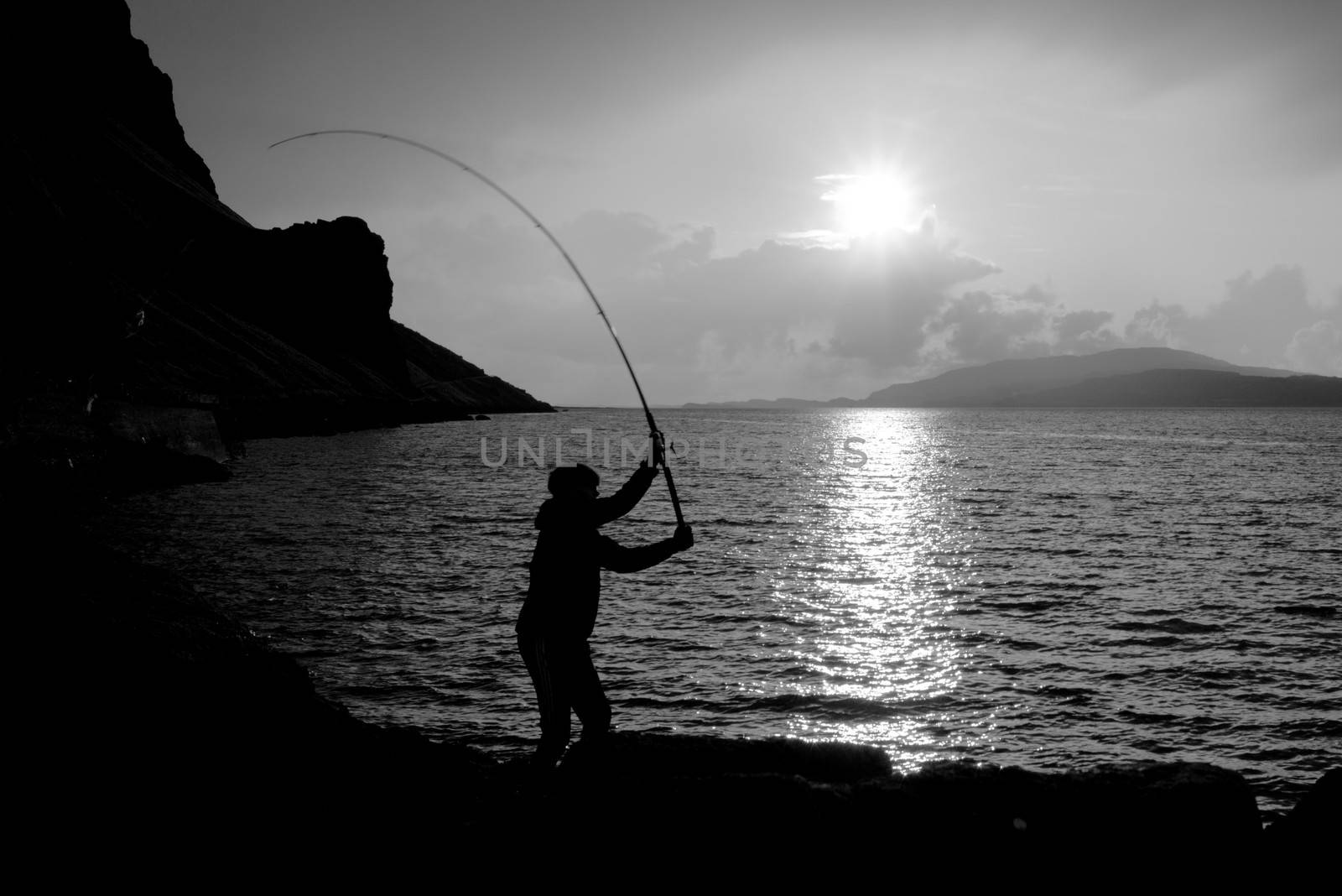 sunsets over loch na keal on the isle of mull as a young man fishes for mackerel in black and white