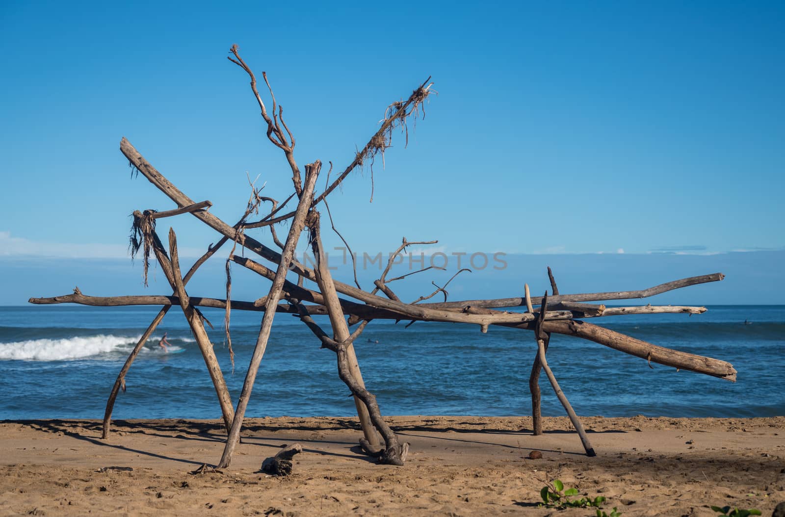 Driftwood structure on Hanalei beach with a surfer visible behind wood