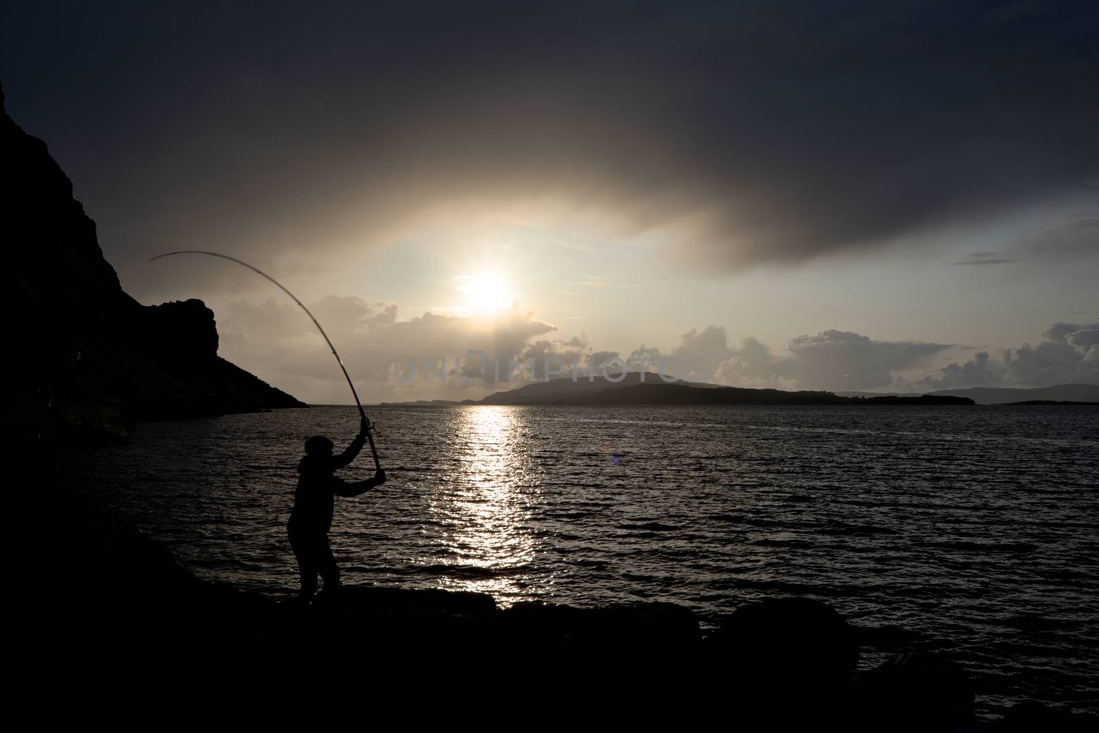 sunsets over loch na keal on the isle of mull as a young man fishes for mackerel in Color