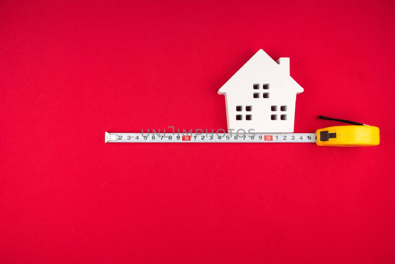 Wooden white house and measuring tape on red background with cop by Bubbers