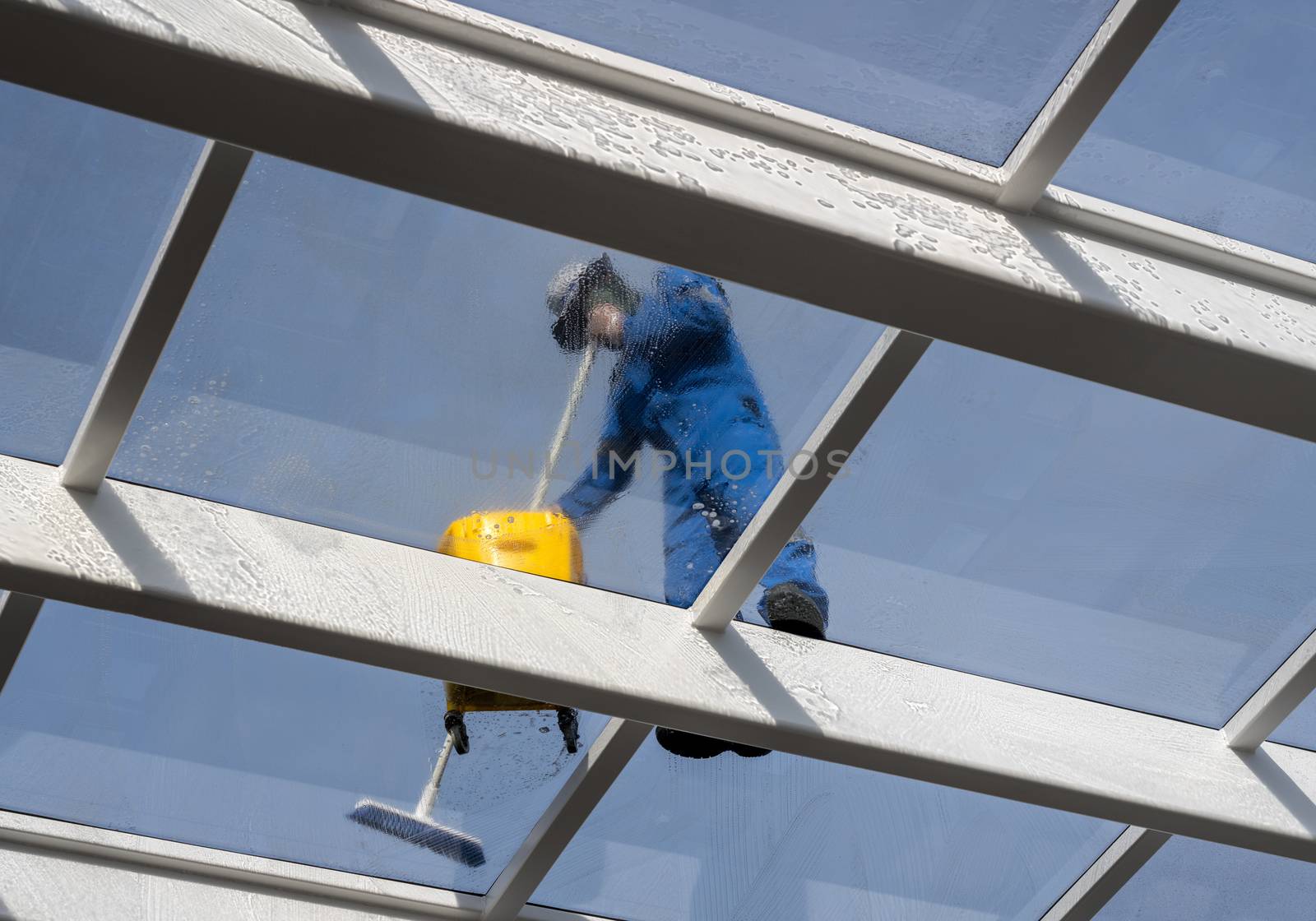 Male worker washing large expanse of glass roof over swimming pool