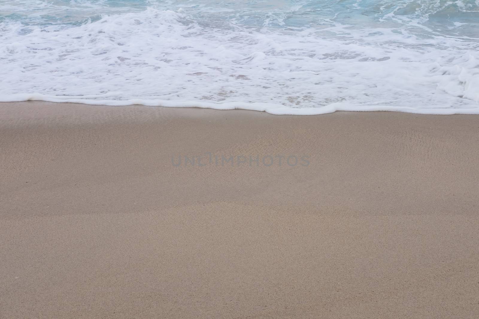 Wave of the sea and white clean foam on the sandy beach by feelartfeelant