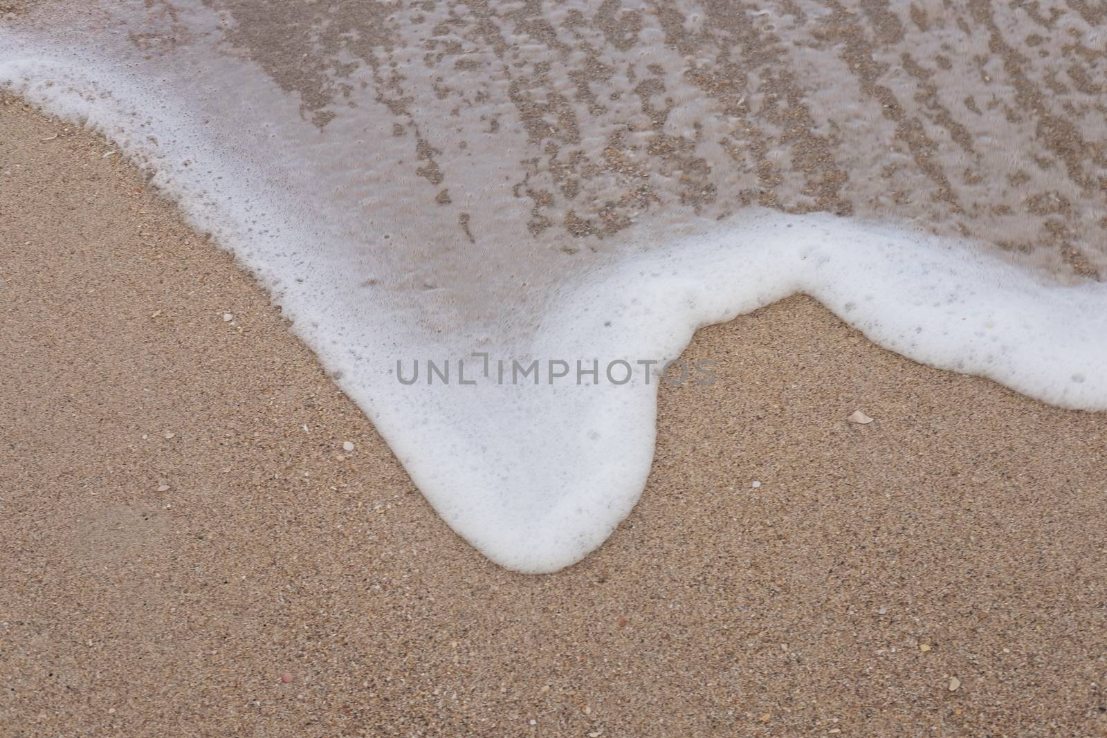 Wave of the sea and white clean foam on the sandy beach by feelartfeelant