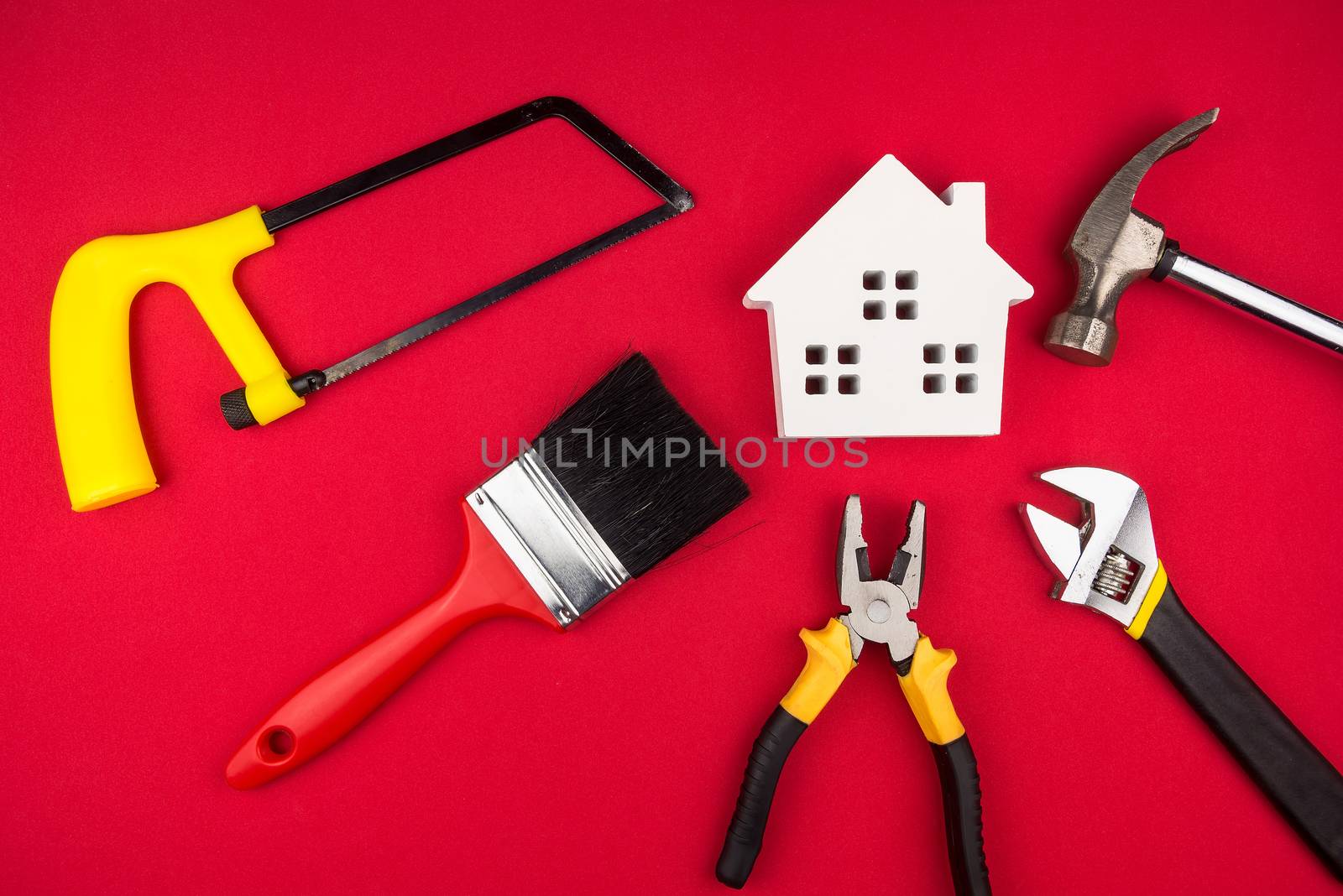 Wooden white house and construction tools on red background with copy space.Real estate concept, New house concept, Finance loan business concept, Repair maintenance concept.