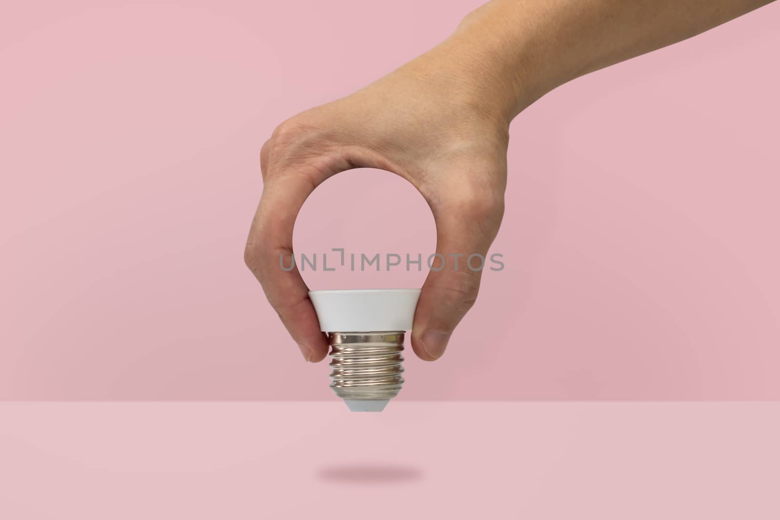 Hand holding a light bulb shape isolated on pink background, min by feelartfeelant