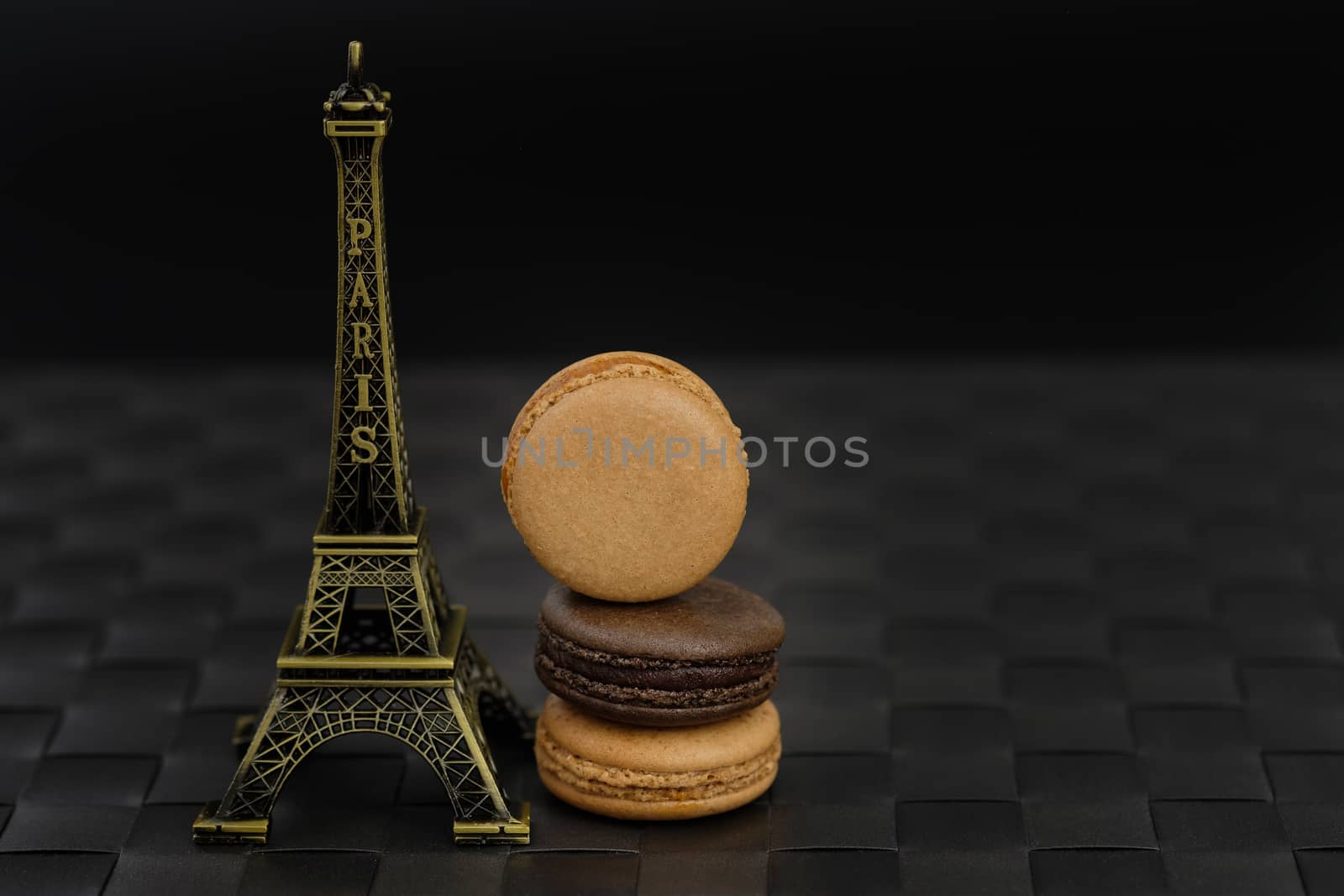 Chocolate and coffee macaroons traditional Parisian cookie and Eiffel tower model on black background in low light.
