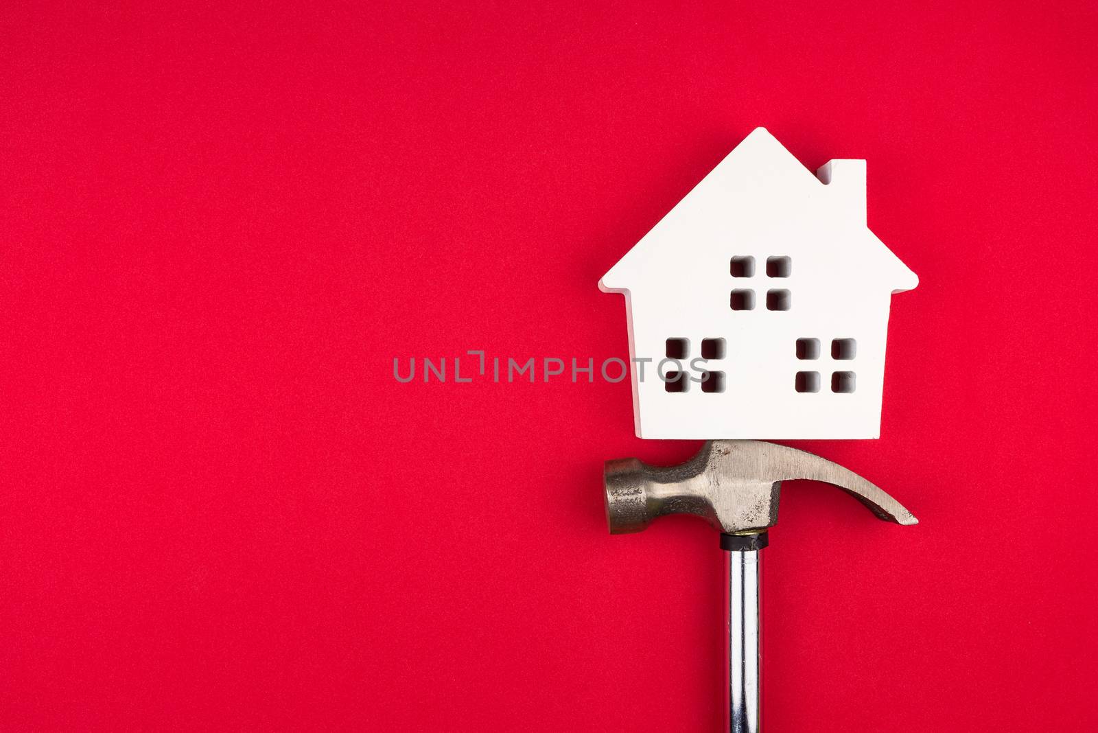 Wooden white house and metal hammer construction tools on red background with copy space.Real estate concept, New house concept, Finance loan business concept, Repair maintenance concept.