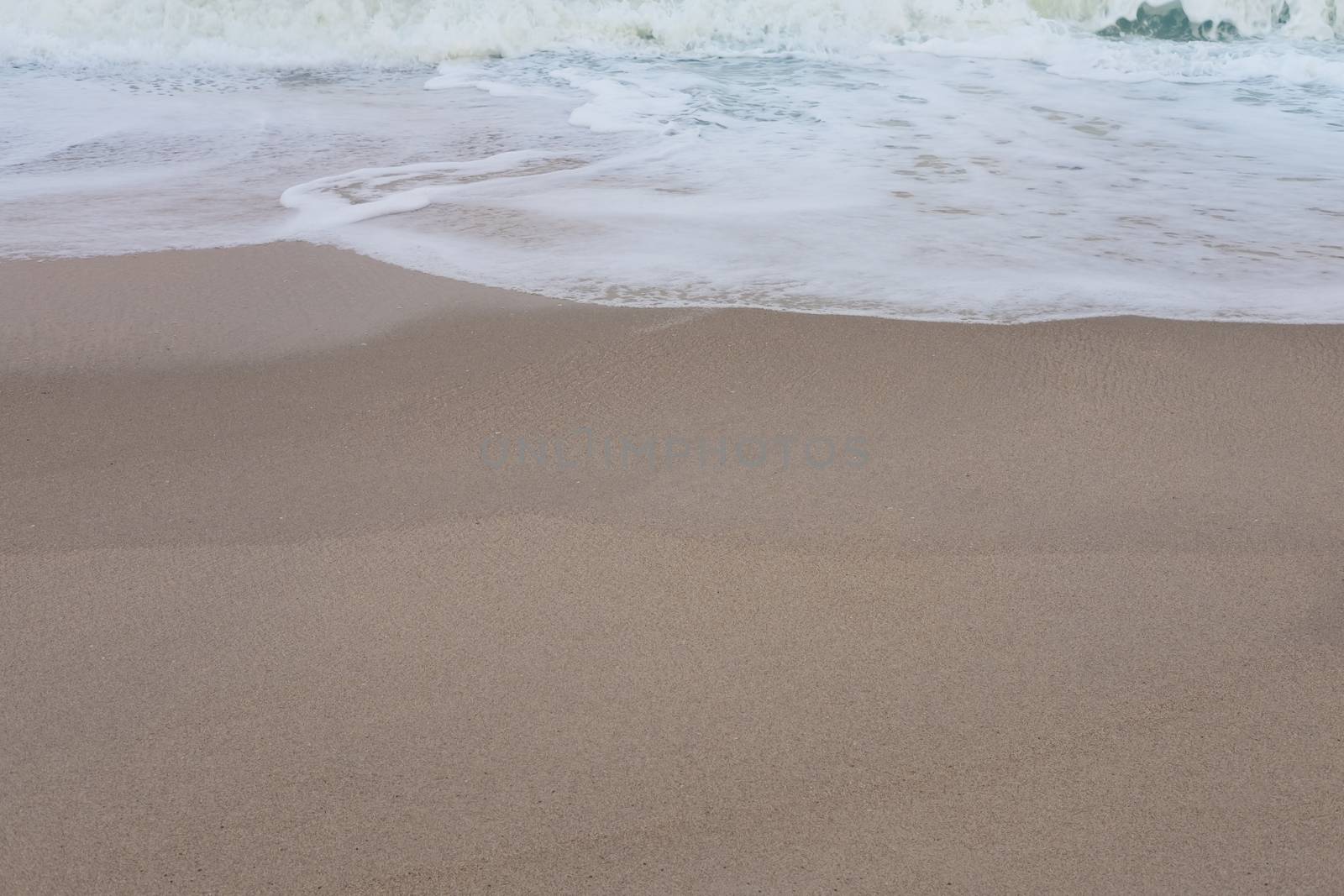 Wave of the sea and white clean foam on the sandy beach by feelartfeelant