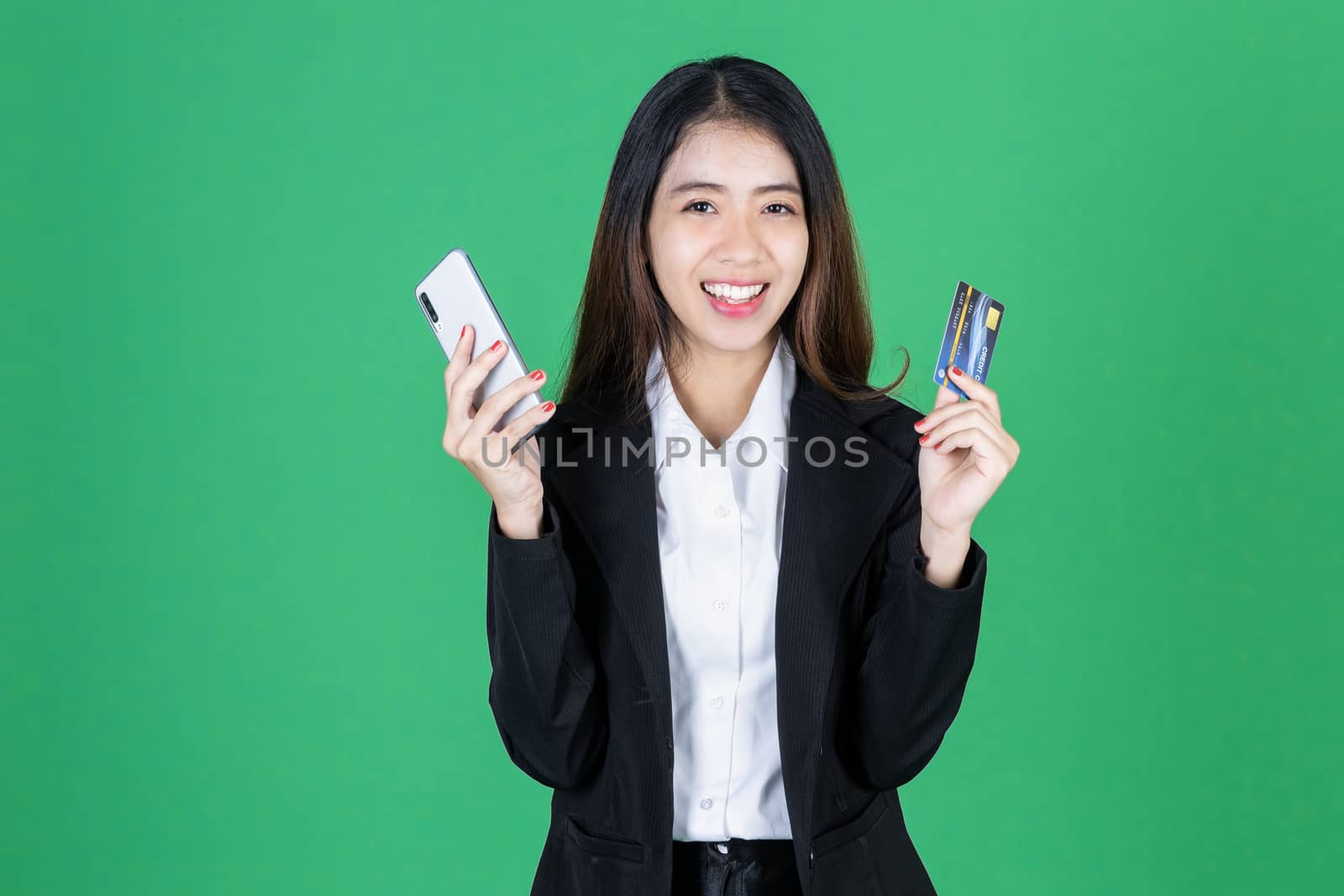 Portrait of cheerful young Asian business woman holding mobile smart phone and credit card on green isolated background.