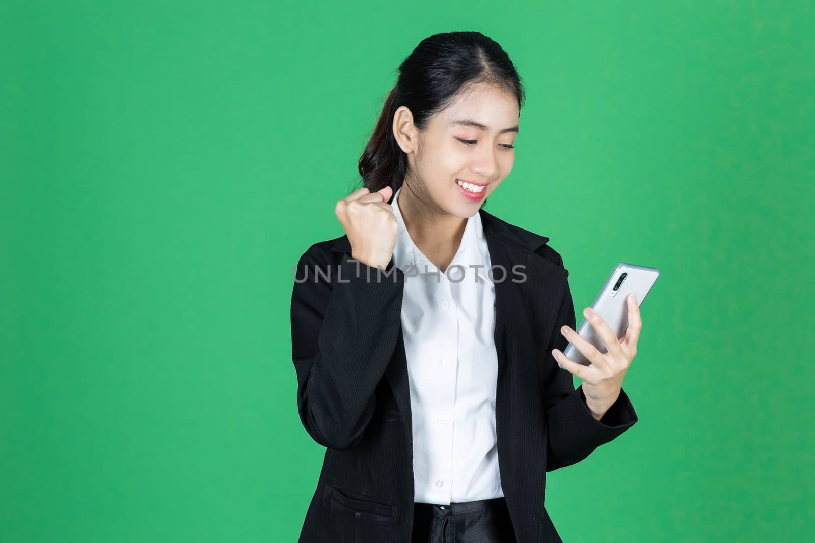 Portrait of cheerful young Asian business woman holding mobile smart phone on green isolated background. by tuaindeed