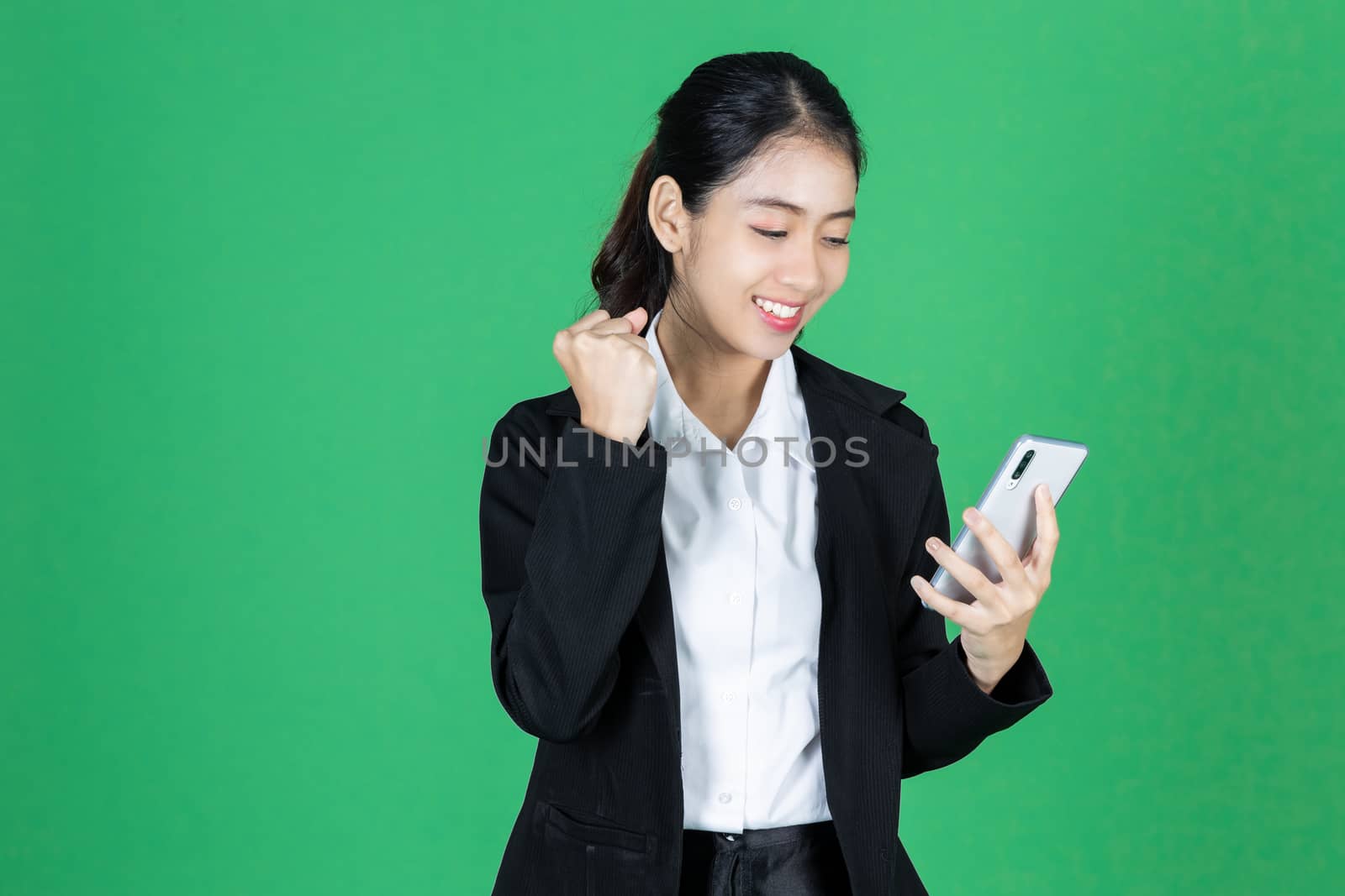 Portrait of cheerful young Asian business woman holding mobile smart phone on green isolated background.