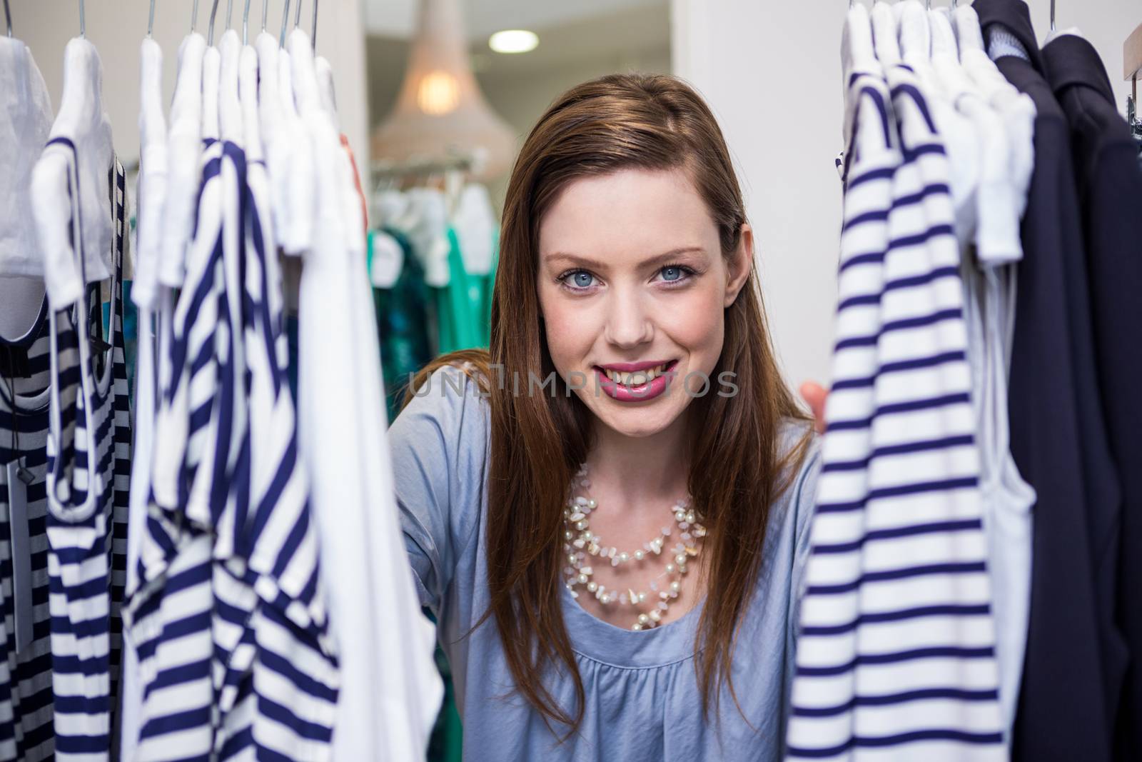 Brunette smiling through clothes rail in fashion boutique