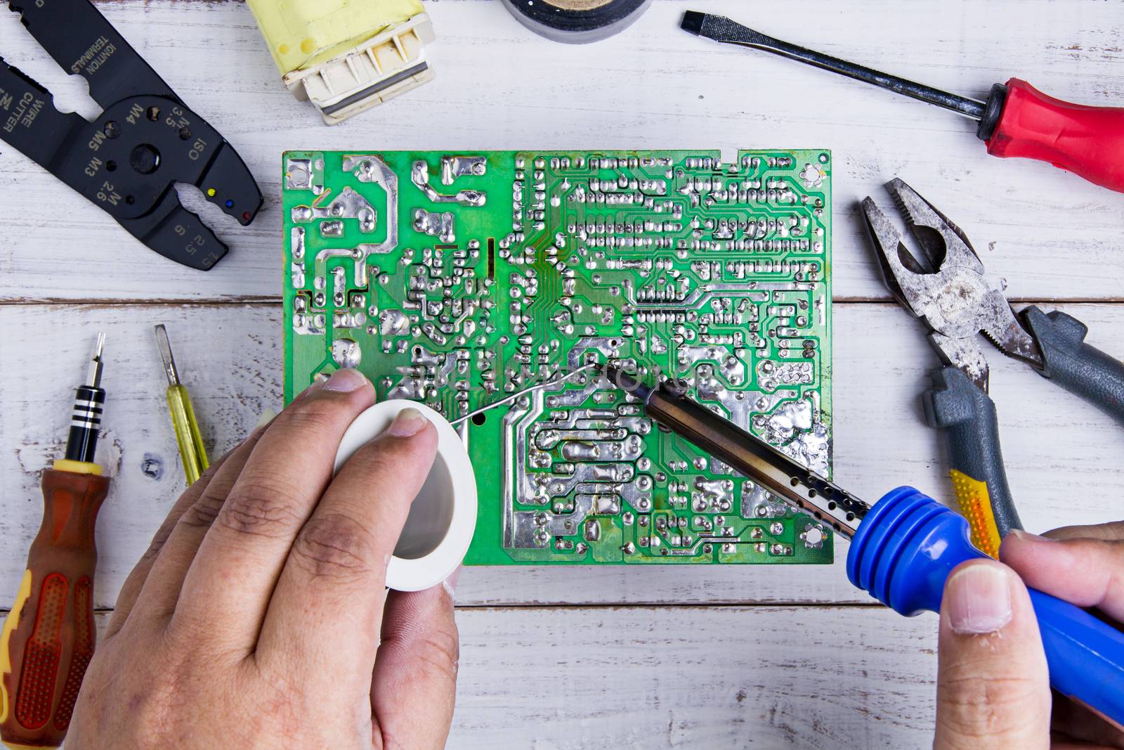 Serviceman soldering circuit board with soldering iron in the service workshop.