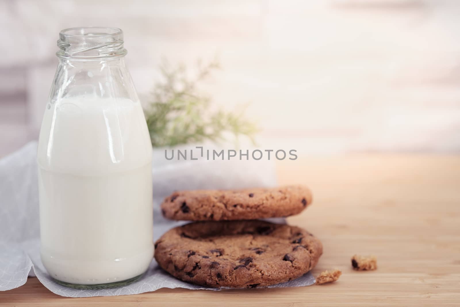 Chocolate chip cookies and a glass of milk on a  wooden table in warm light, Vintage look.